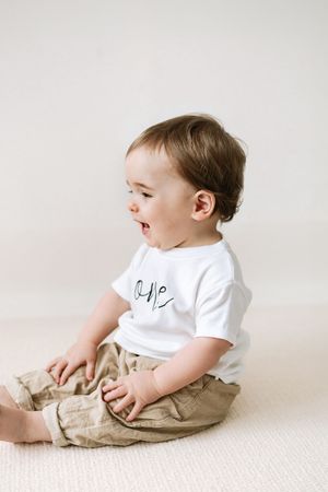 Cute baby wearing a white 'one' birthday t-shirt  sitting on a cream floor Nottingham first birthday photoshoot