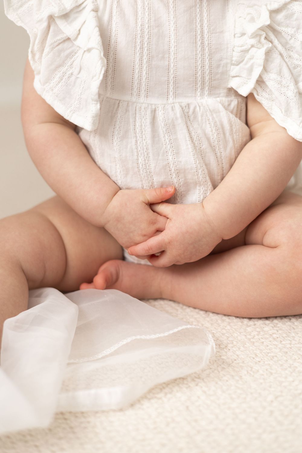 Close-up of a baby in a white ruffled romper sitting cross-legged on a cream knit blanket Nottingham first birthday photoshoot