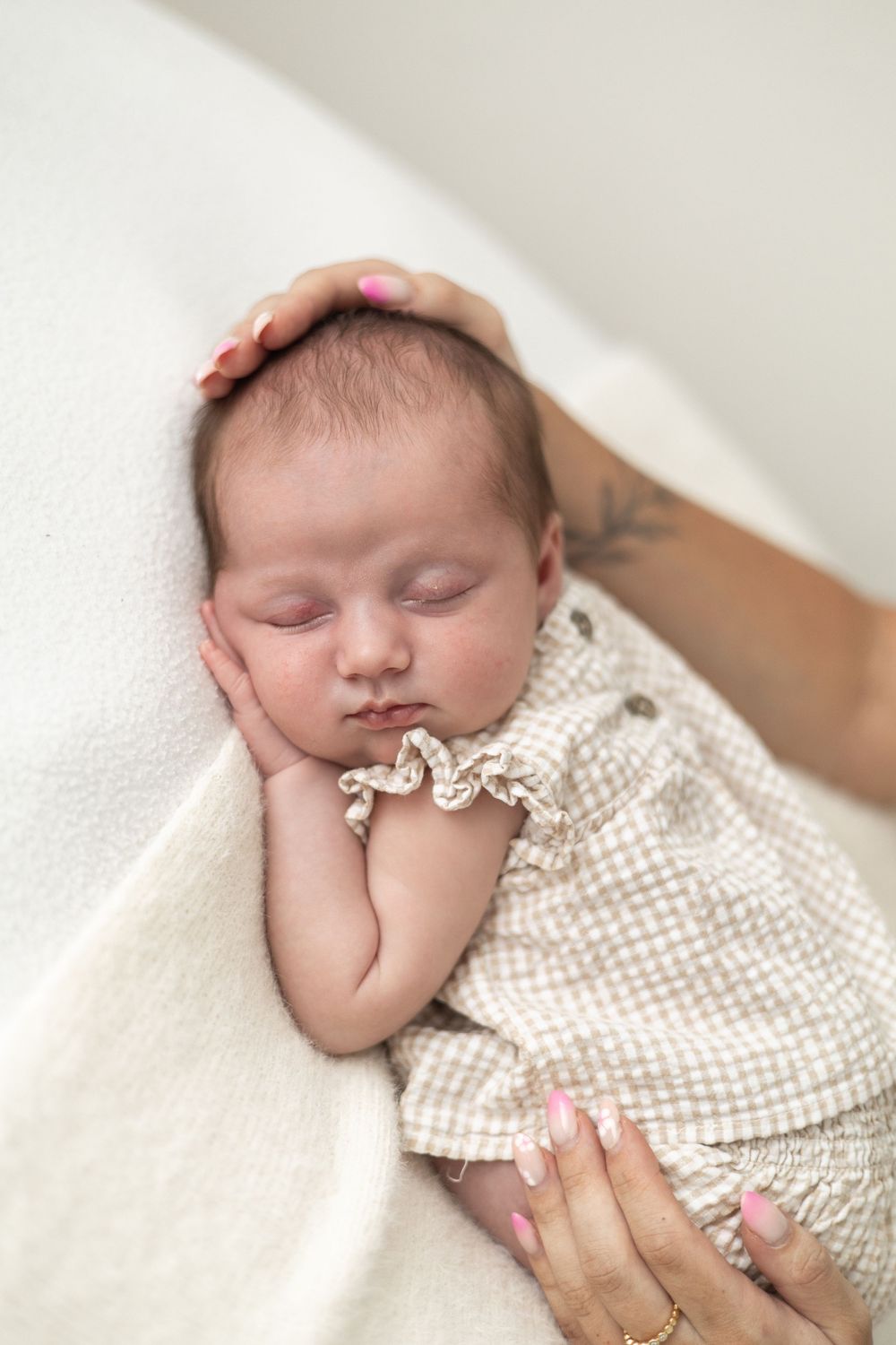 Peaceful newborn baby girl sleeping on white blanket while mother gently holds her head Nottingham newborn photography portrait.
