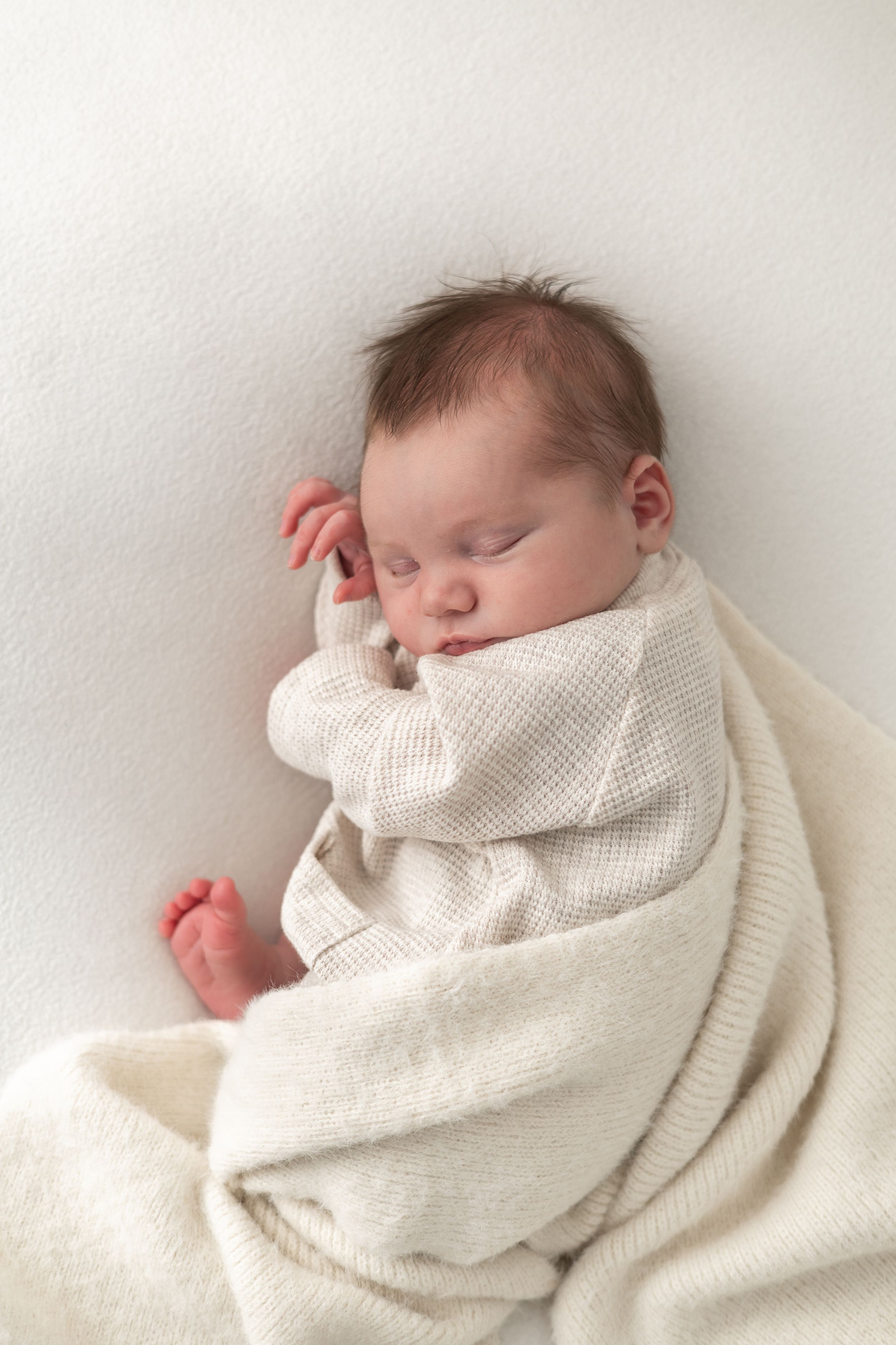 Peaceful newborn baby sleeping wrapped in a soft cream knit blanket on a white background newborn photographer Nottingham cosy home studio