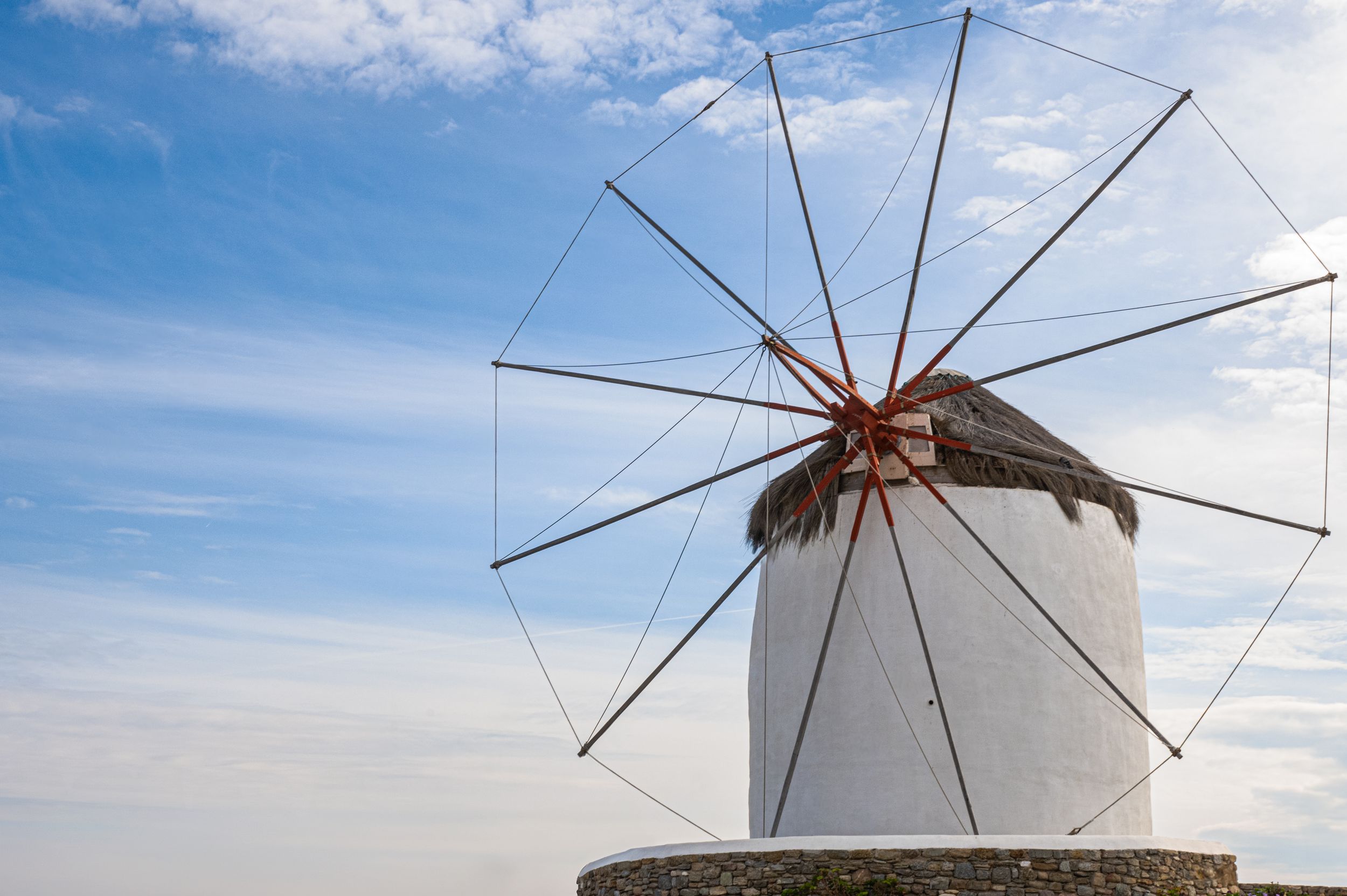 Traditional white windmills stand in a row against a blue sky on a sunny day in Mykonos, Greece.