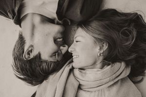 Two people share a tender kiss while lying down together in black and white photography.