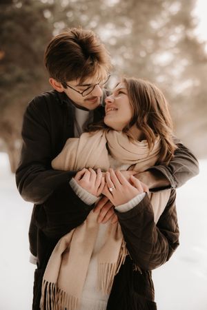 A romantic winter couple embraces outdoors in warm clothing with a soft, dreamy sepia-toned background.
