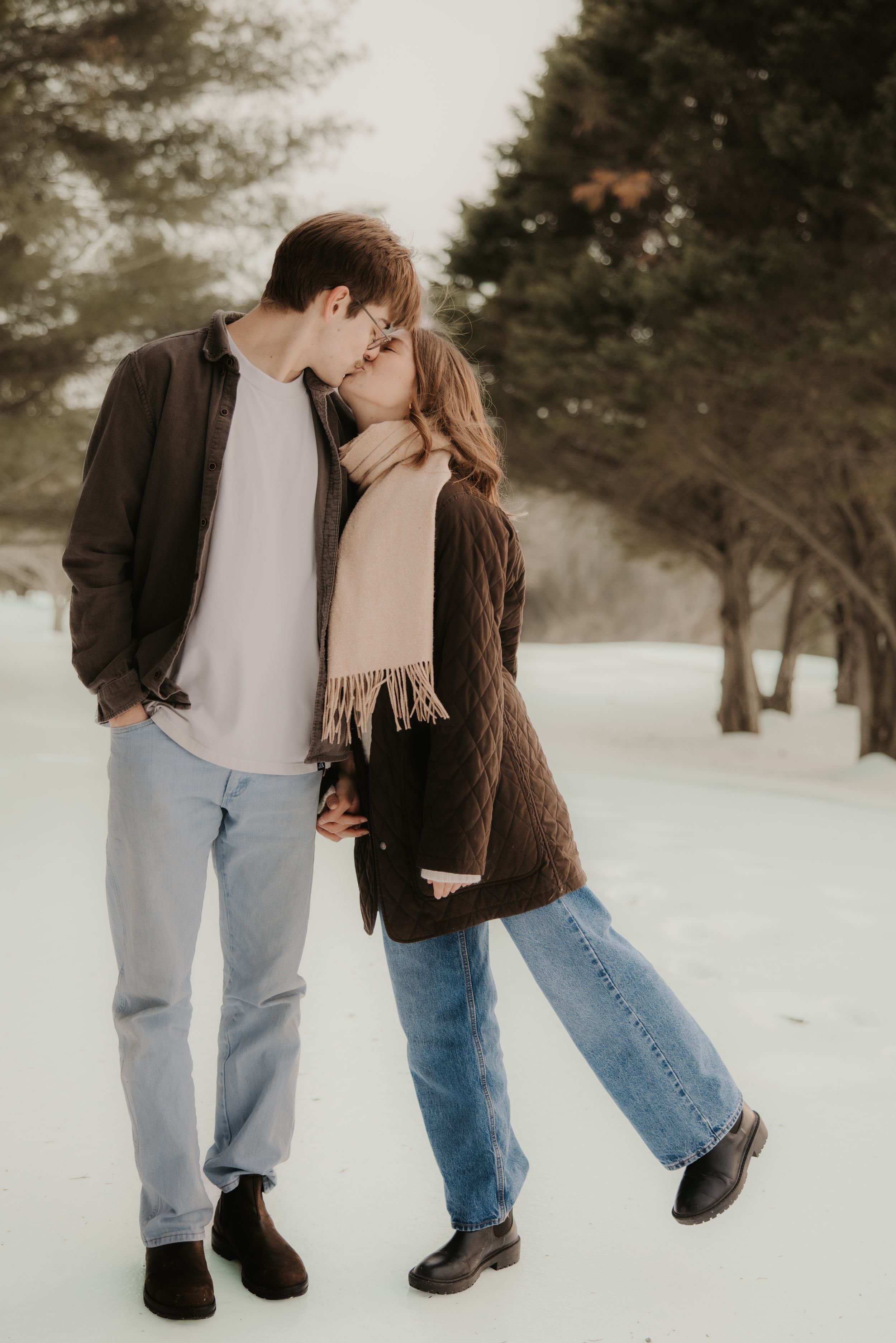 A romantic couple embraces in a snowy winter landscape wearing casual clothing and warm layers.