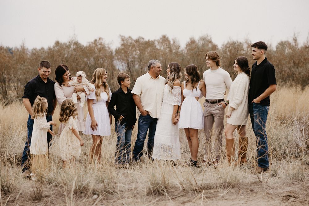 A group of people wearing white and neutral colored clothing walk together through a golden field at sunset.