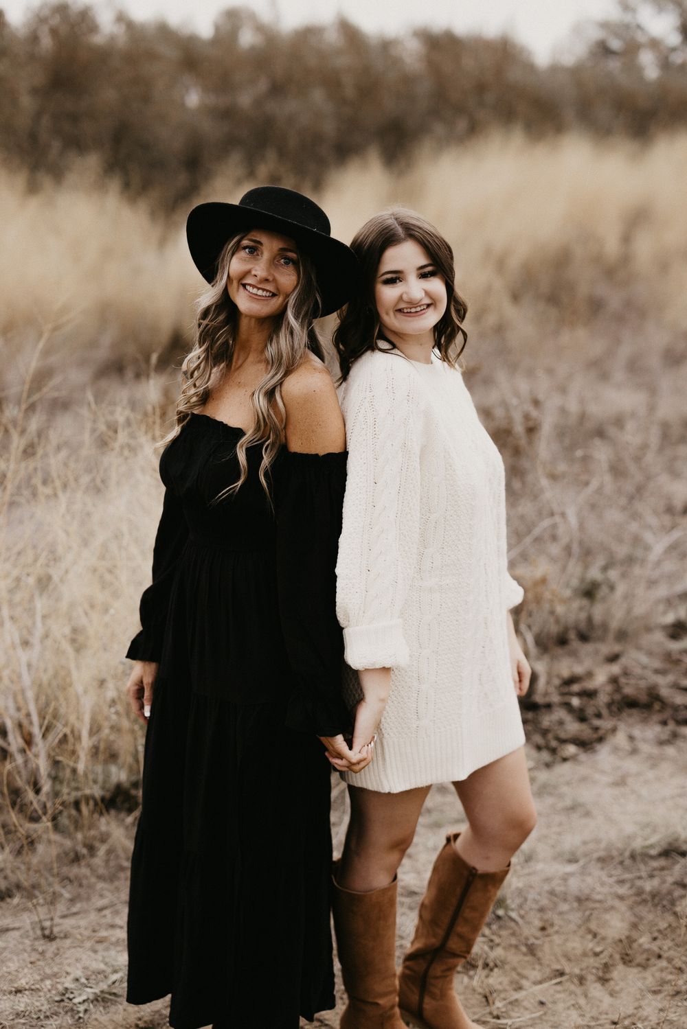 Two friends in contrasting outfits of black and white share candid laughs in a rustic outdoor setting.