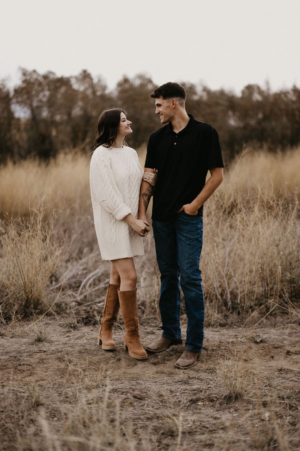 A couple shares a romantic moment together in a field of dried grass during golden hour.
