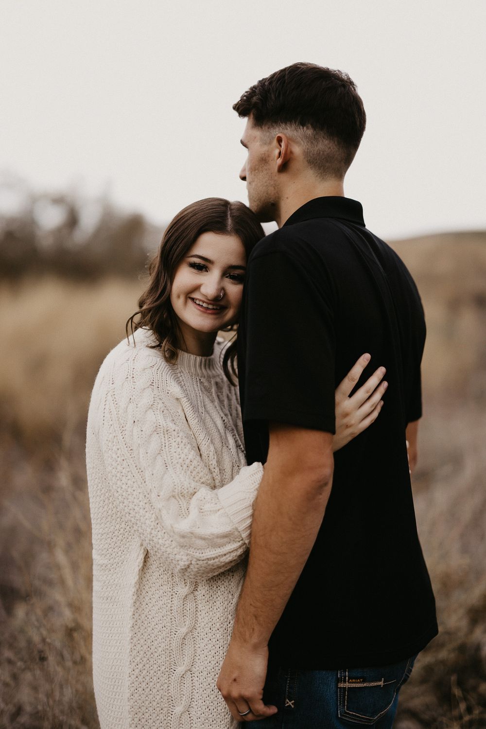 A couple shares intimate moments in a field wearing coordinated casual outfits of black and cream.