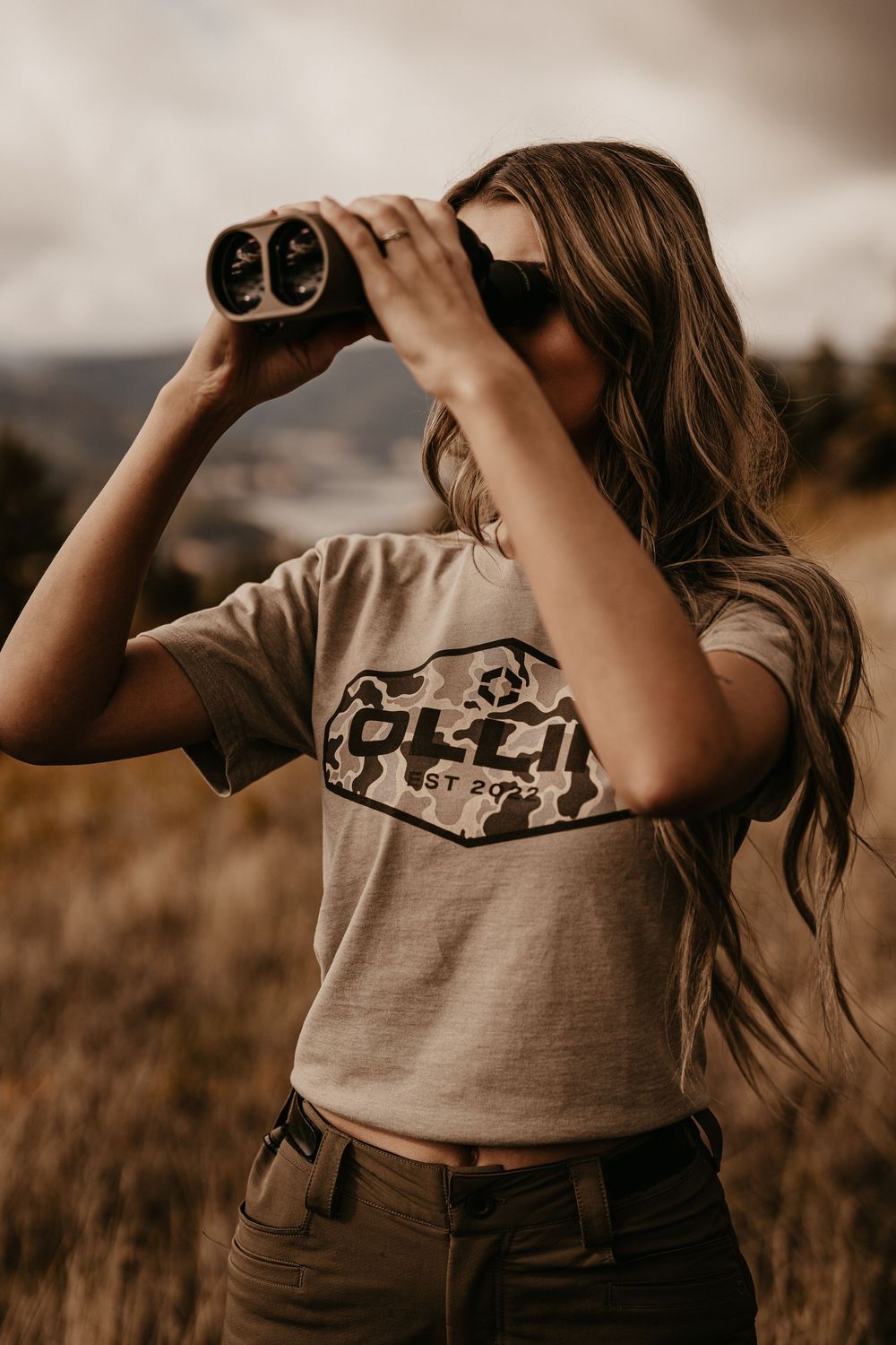 Person looking through binoculars in a desert landscape during golden hour.