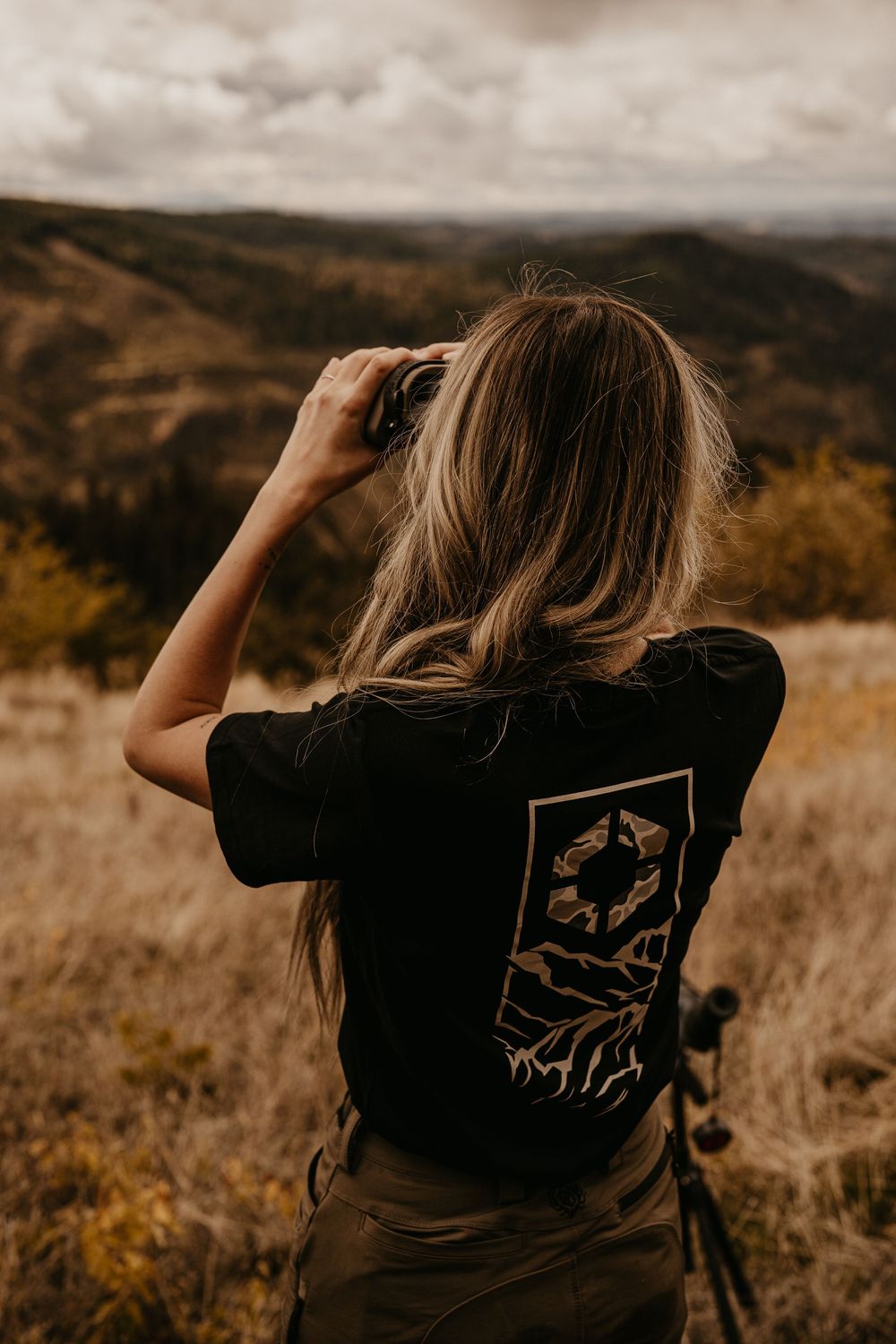 Person looking through binoculars in a mountainous landscape during autumn.