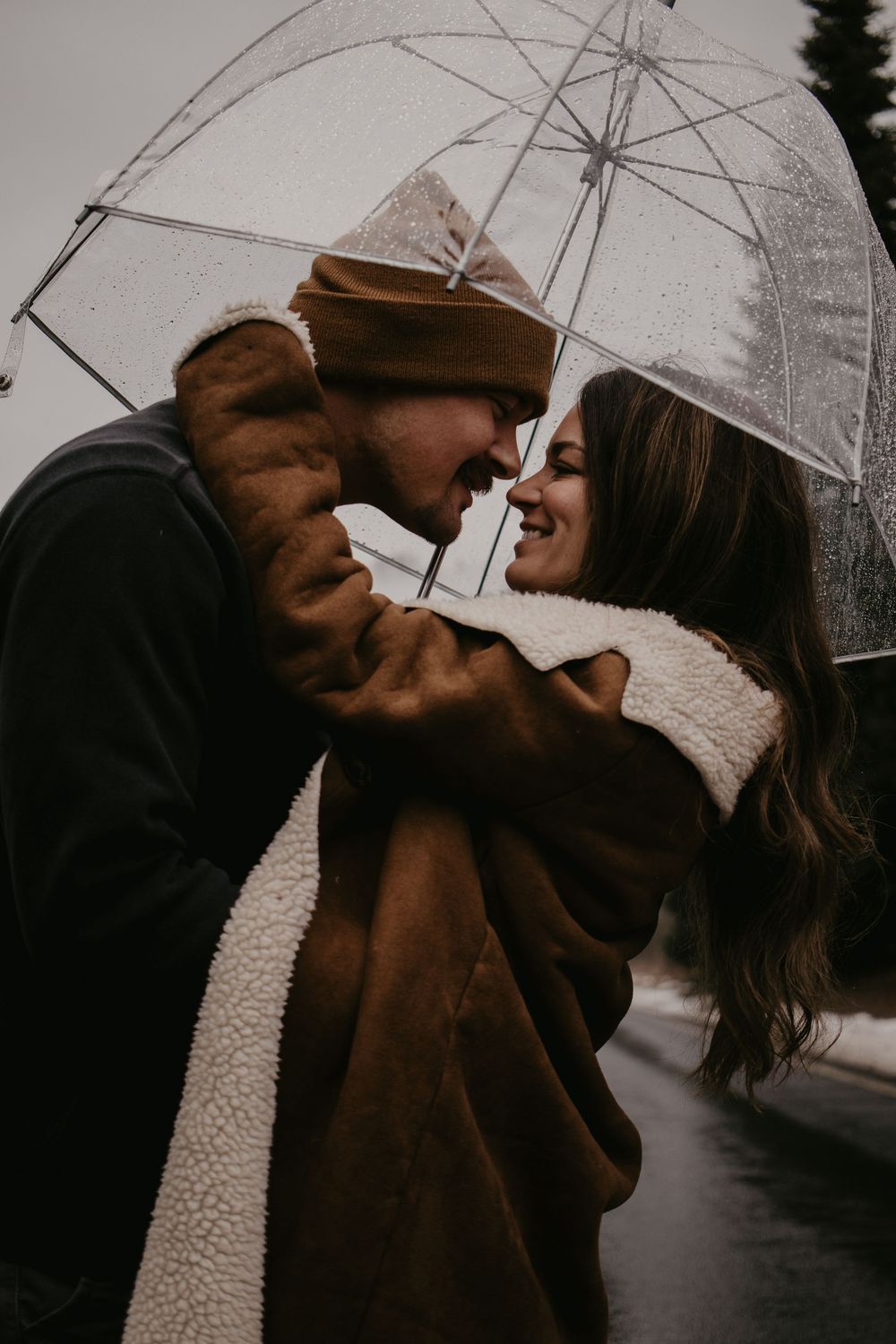 Couple sharing tender moment under clear umbrella in winter weather.