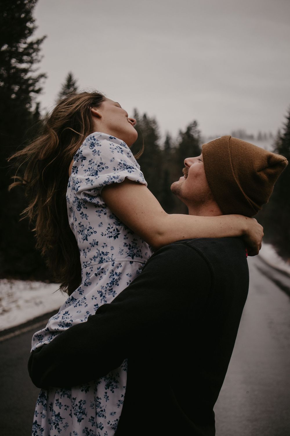 Couple sharing playful moment on wet road with forest backdrop.