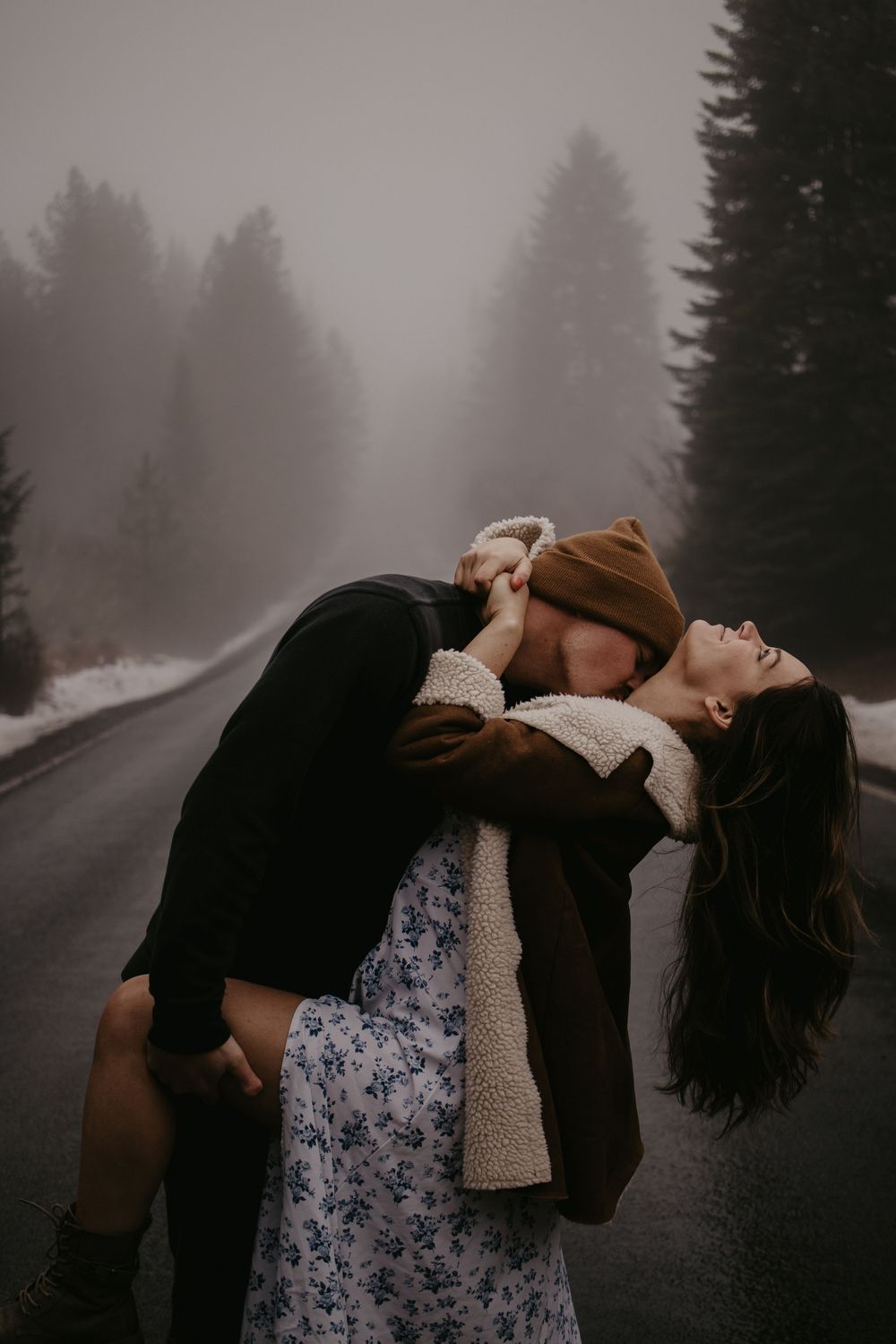 A romantic moment captured in moody fog on a misty forest road.