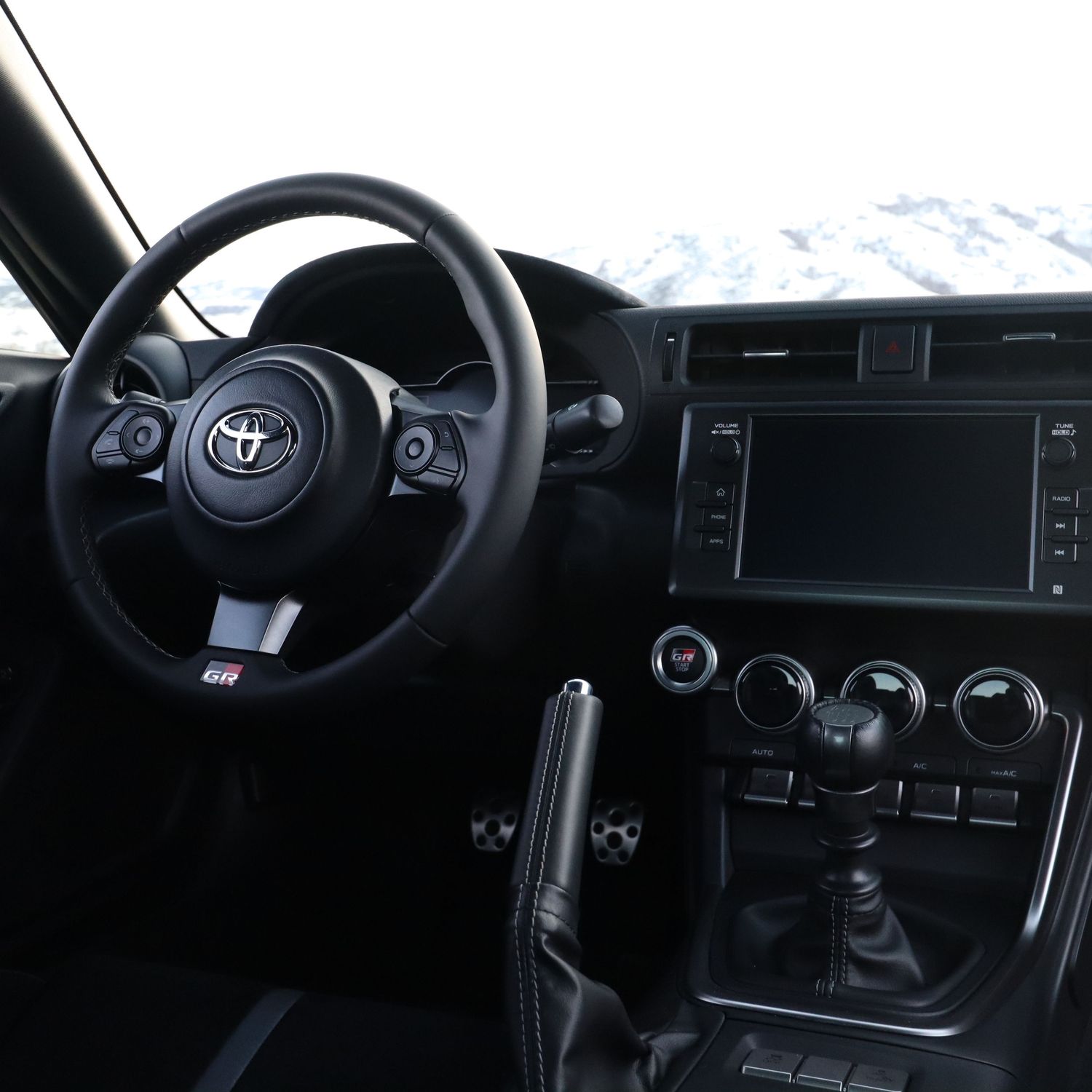 Interior view of a Toyota GR sports car featuring black leather seats, manual gearshift, and touchscreen infotainment system.