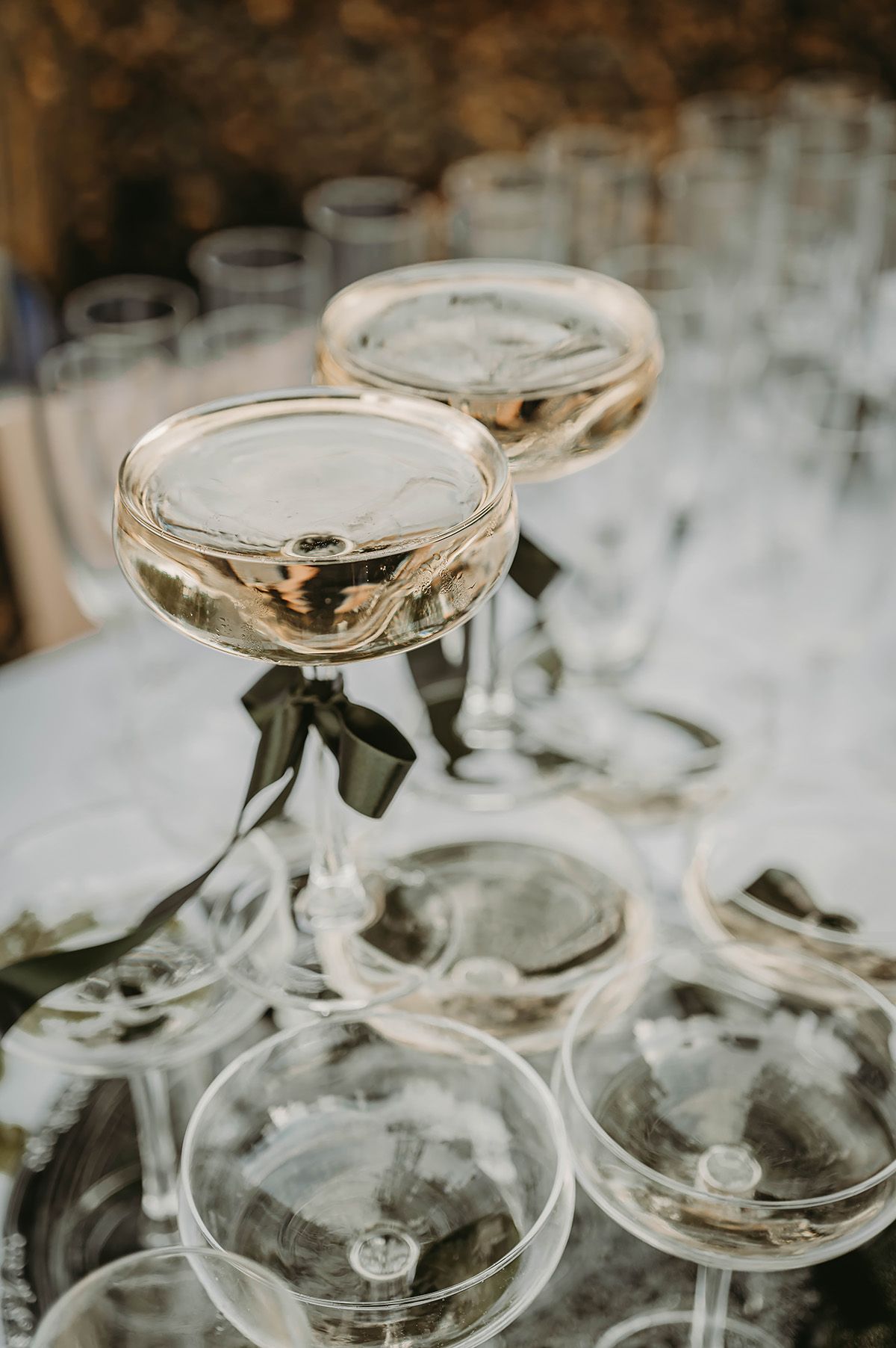 Champagnetorn med två glas i topp, dekorerade med gröna sidenband.Bröllopsfotograf Lets Bloom Media i Norrköping.