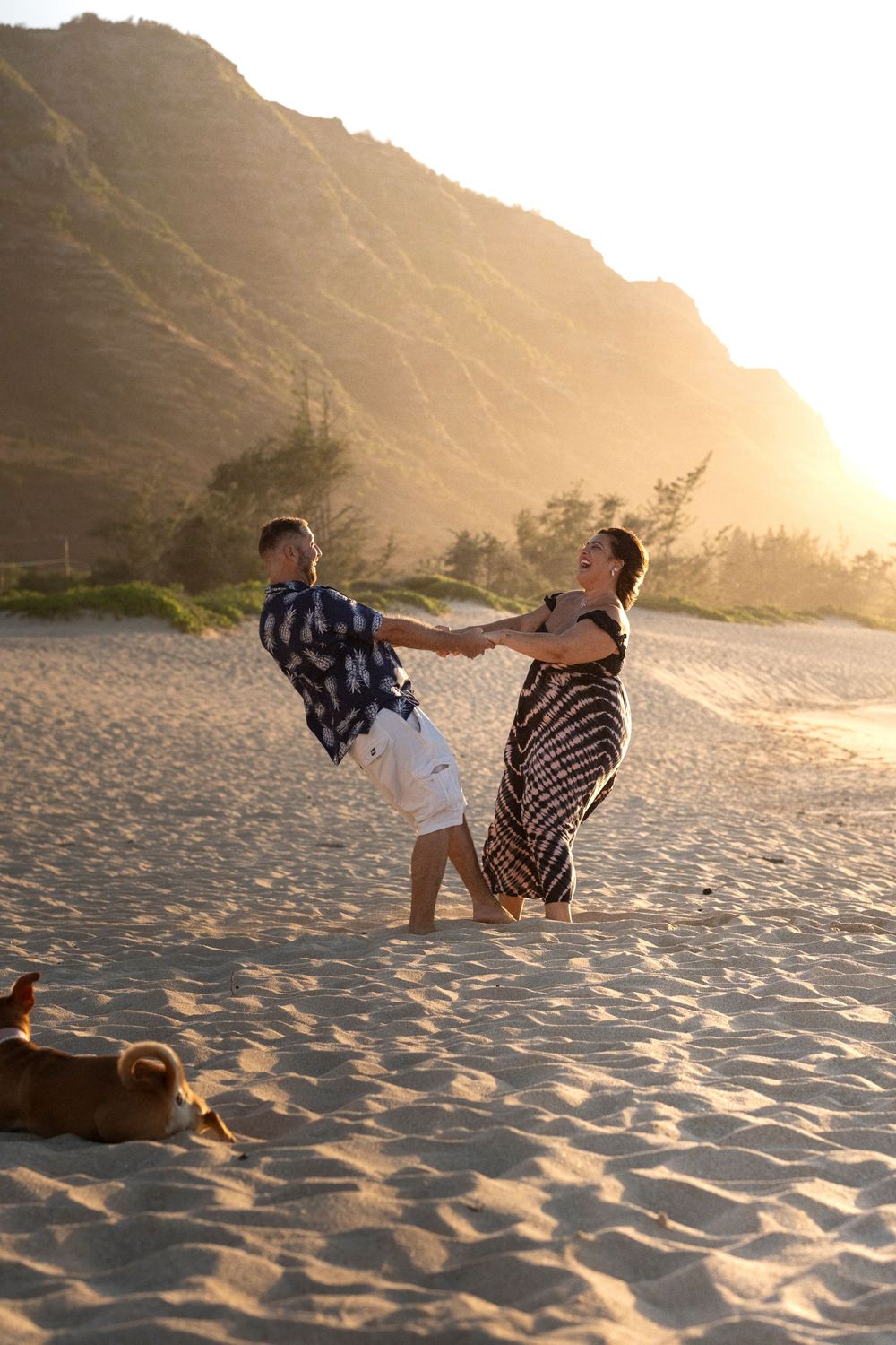 Couple dancing playfully on a North Shore Oahu beach during a sunset photography session with their dog nearby.