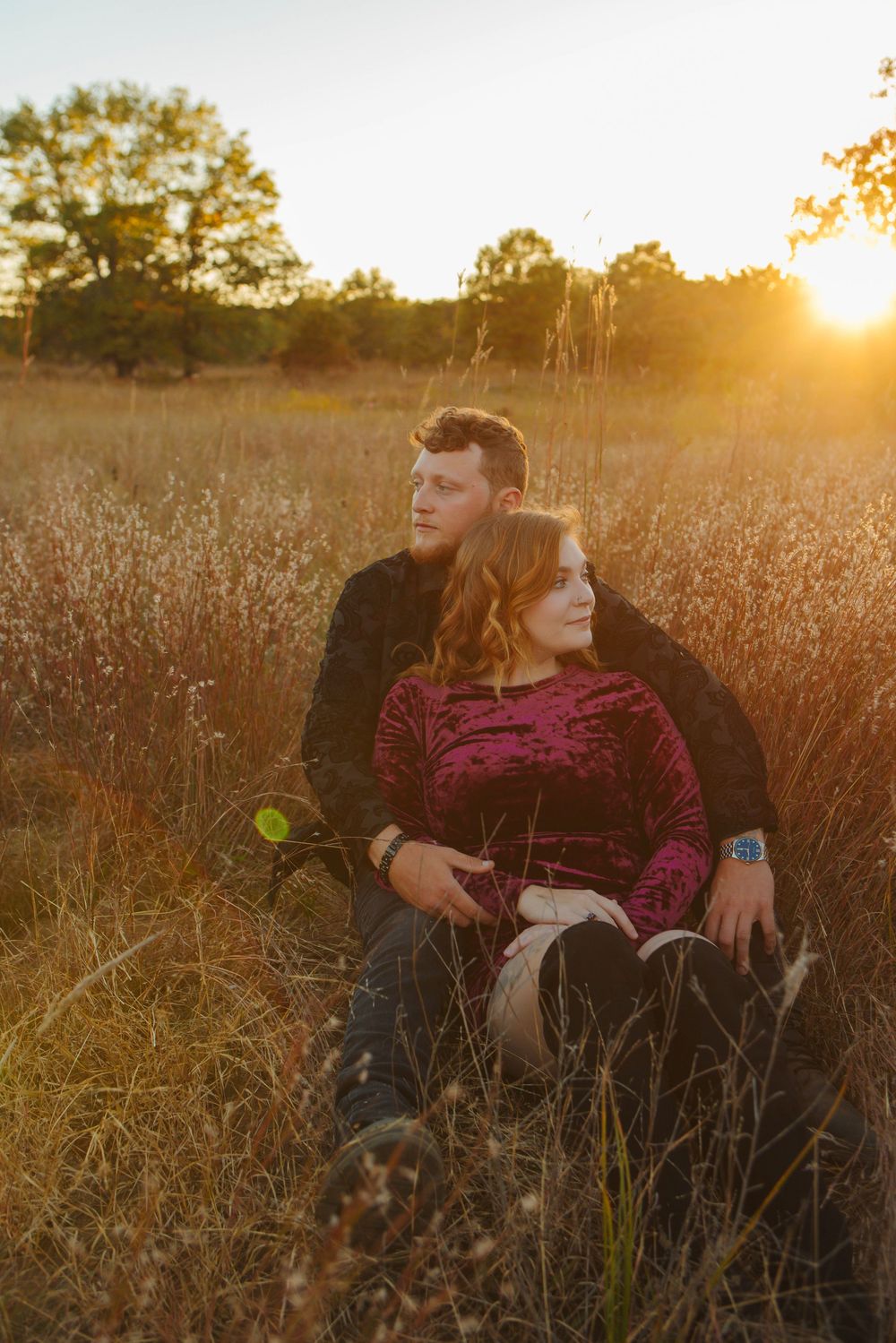 A couple sits together in a golden wheat field at sunset as warm sunlight illuminates the peaceful autumn scene.