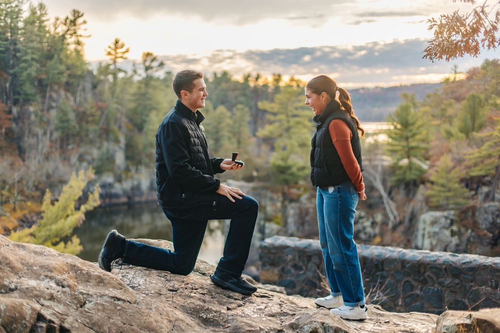 Two people share a special moment during a sunset proposal on a scenic cliff overlooking autumn wilderness.