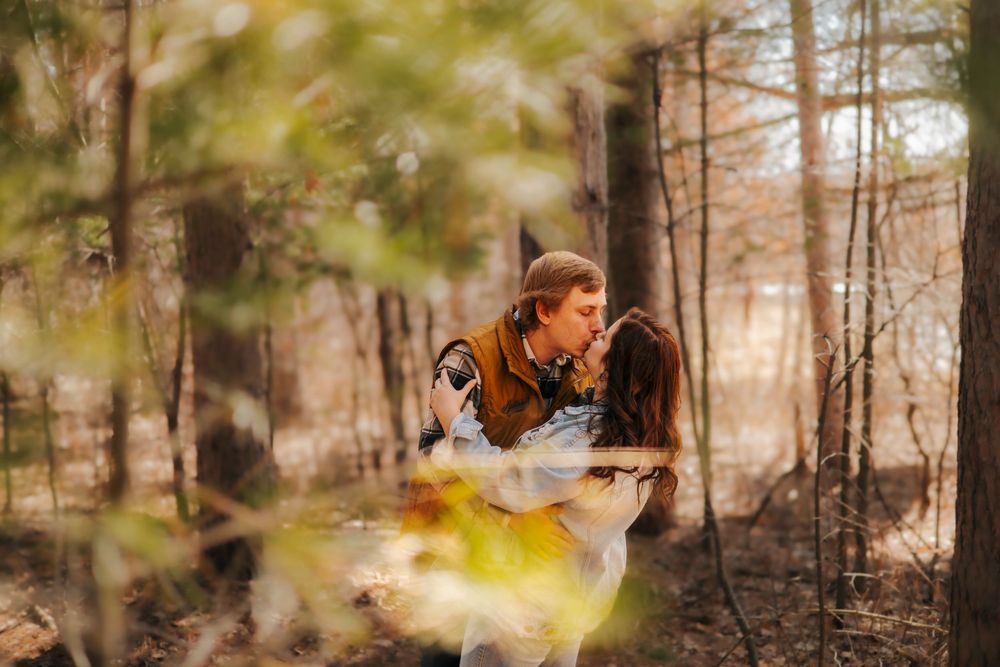 Couple sharing a romantic kiss in a sunlit autumn forest surrounded by colorful foliage.
