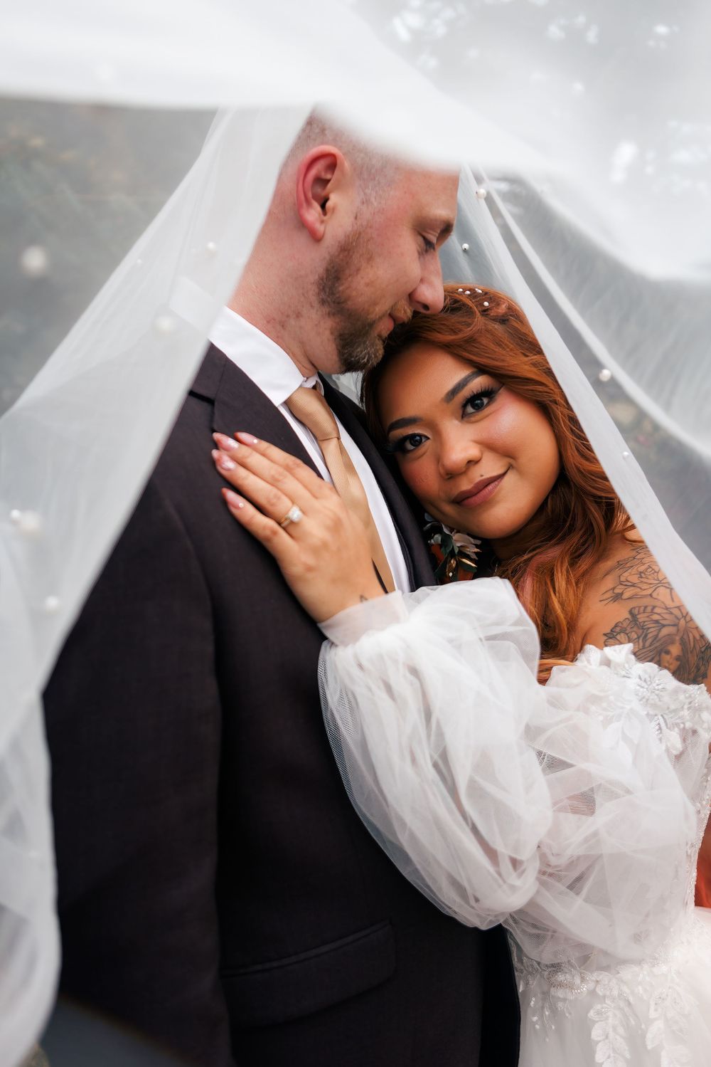 Bride and groom share a romantic moment under a flowing veil on their wedding day.