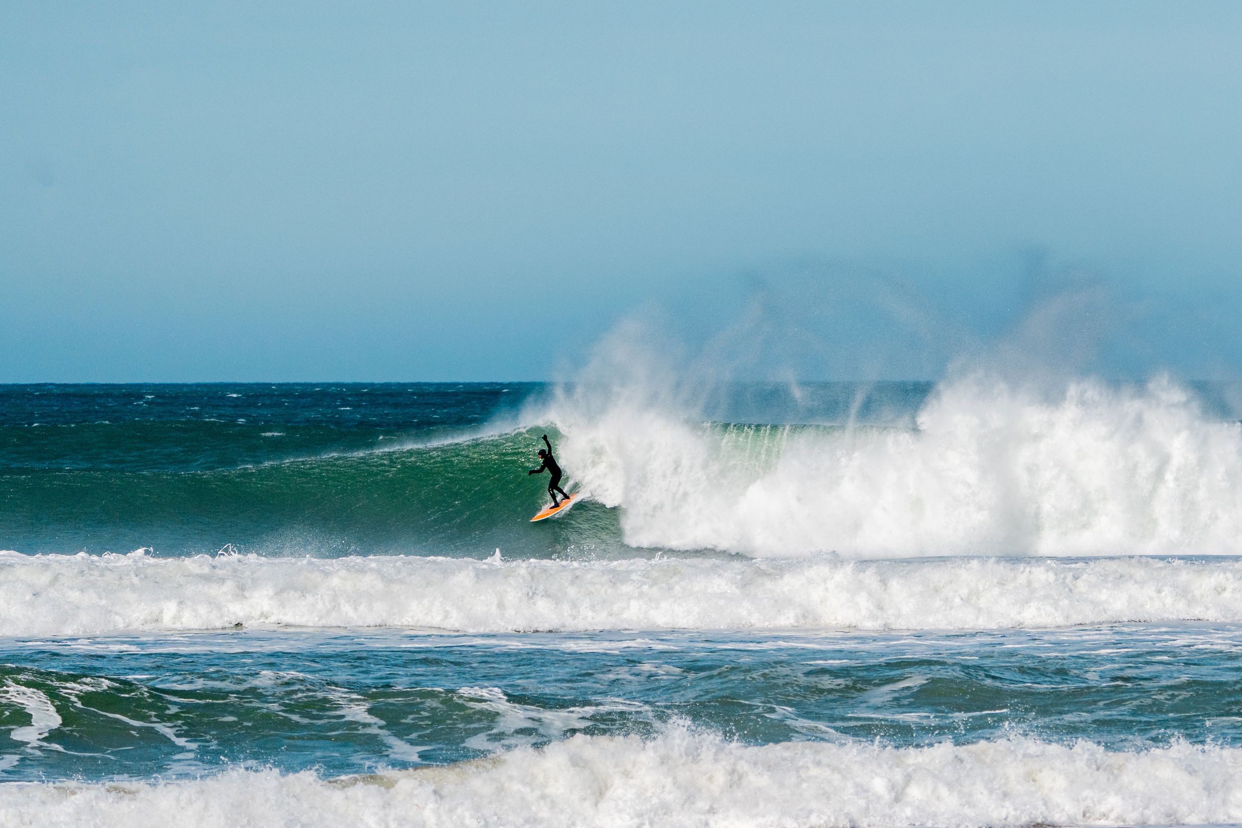 Dynamic surfing action shot showing rider navigating through large breaking wave with ocean spray.