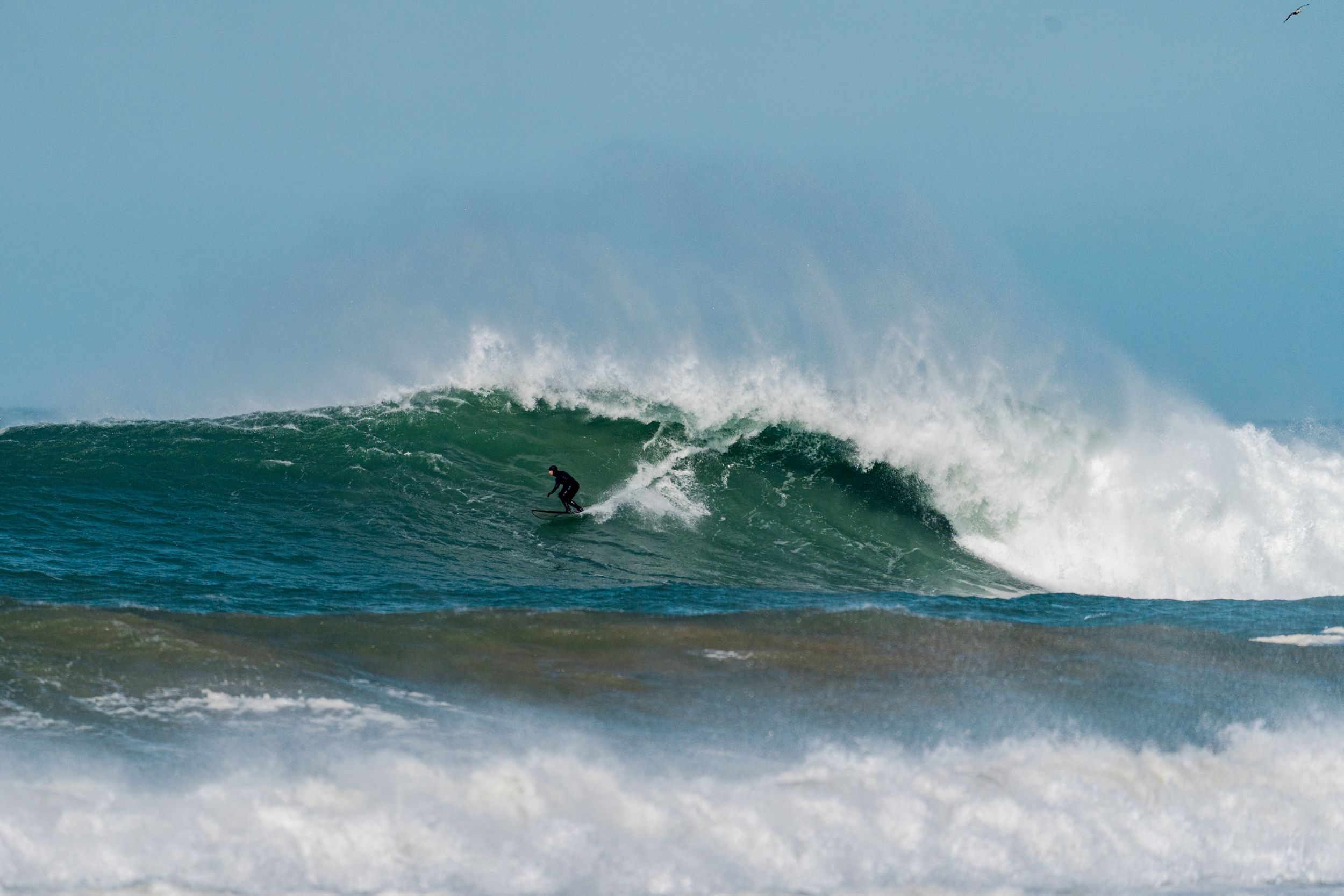 Surfer carves through massive turquoise wave with white water spraying in tropical setting.