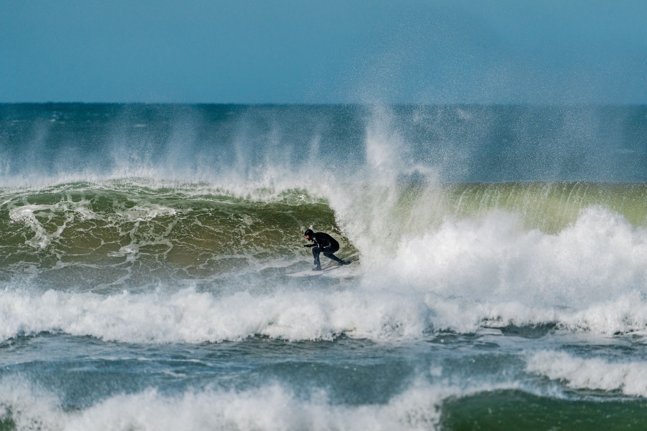 Silhouetted surfer carving through a massive breaking wave with spray flying in the air.
