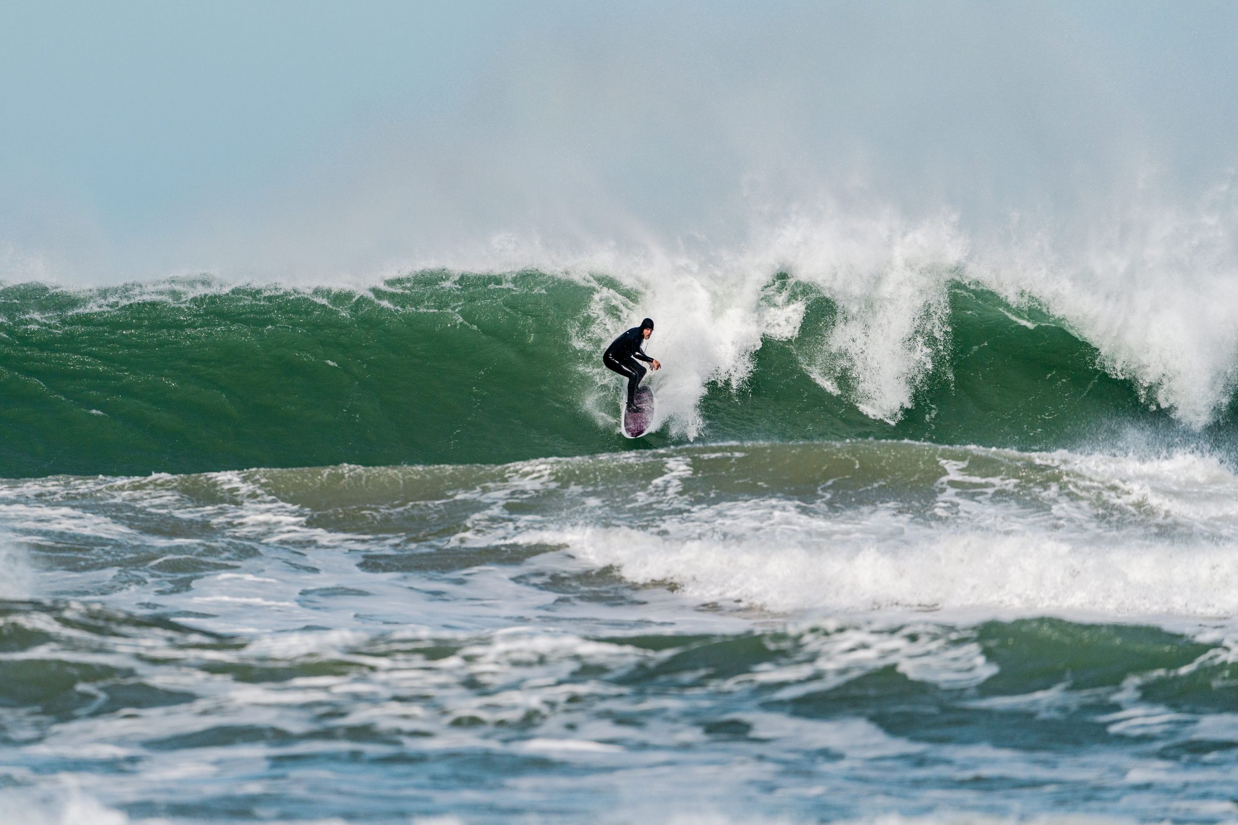 A surfer rides a large green wave while performing a skilled aerial maneuver in the ocean.