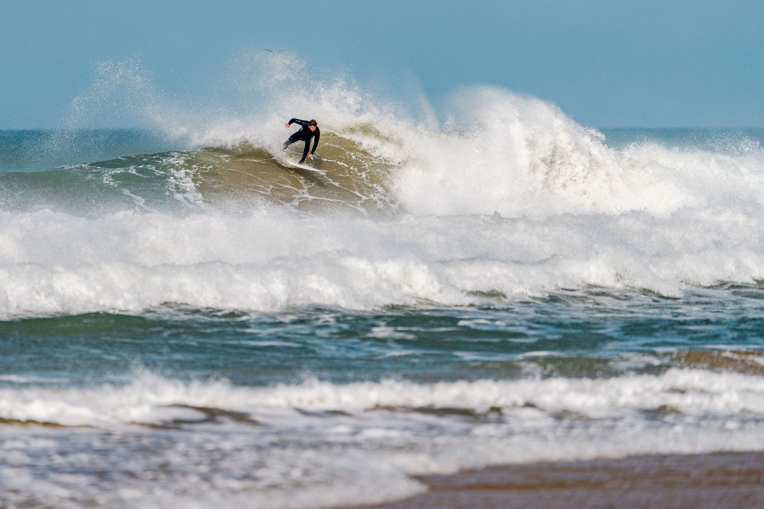 A silhouetted surfer navigates the crest of a breaking wave against a misty ocean backdrop.