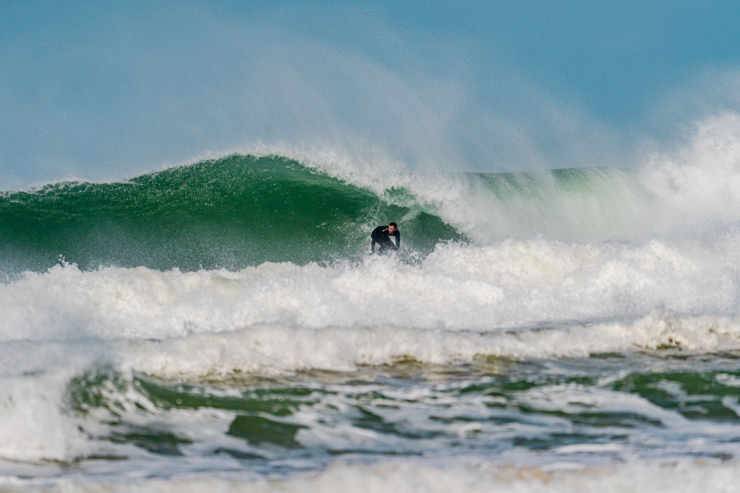 Surfer navigating through a powerful green wave with white foam spraying in the ocean.