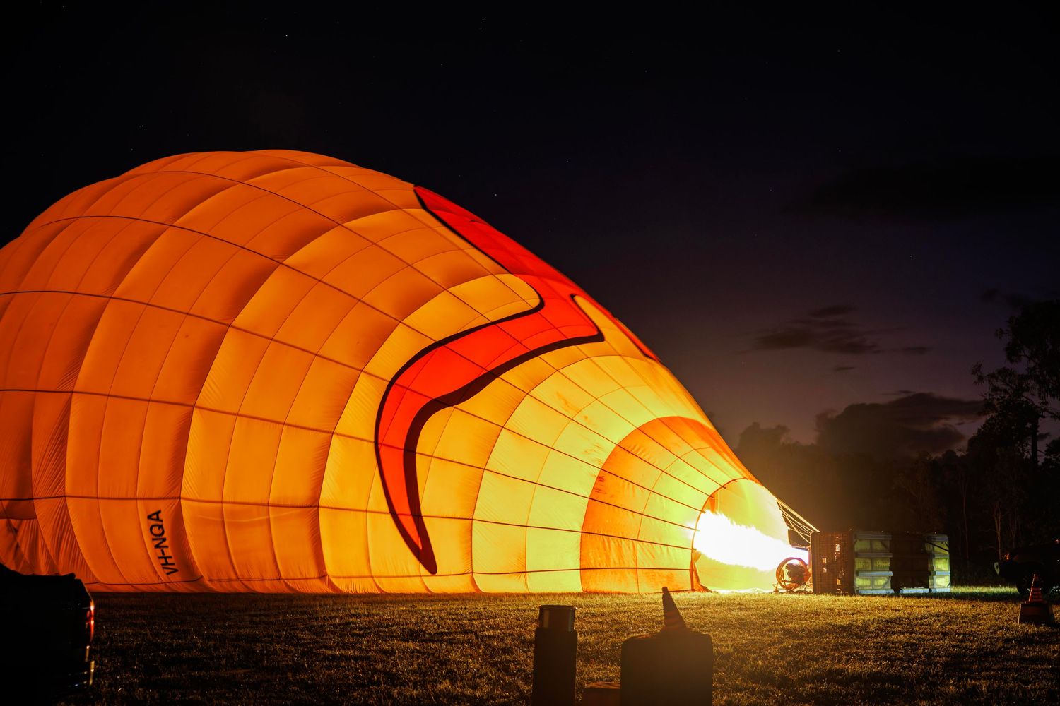 A glowing orange hot air balloon being inflated at night with a bright flame bursting from its opening on a dark field. Cairns, Australia