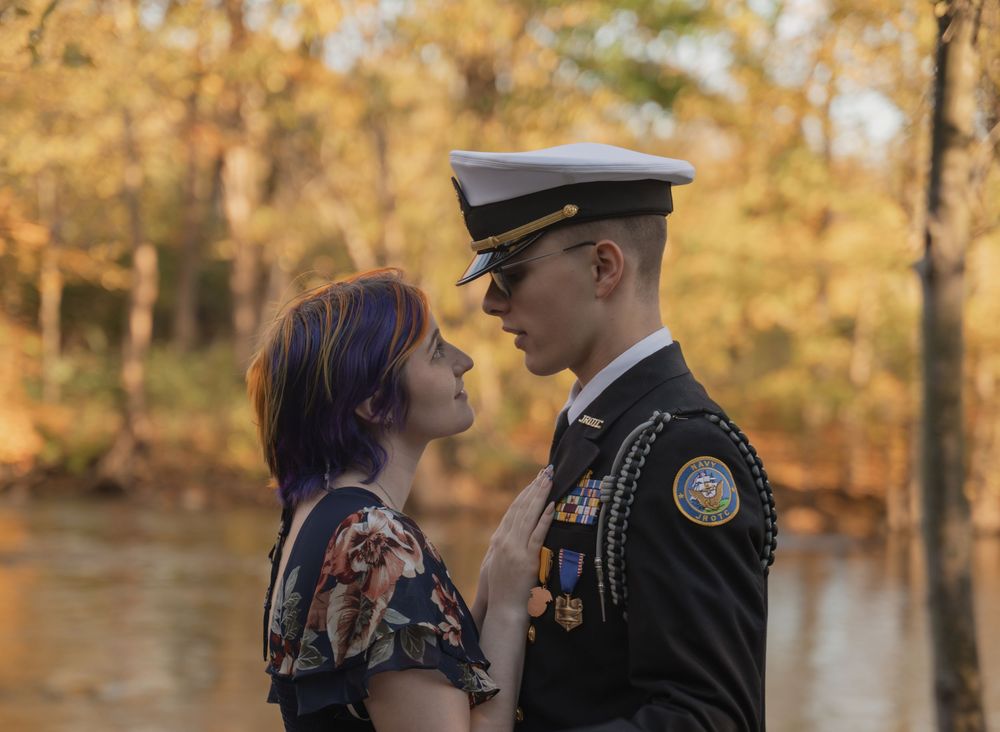 Military cadet in dress uniform sharing romantic moment with girlfriend amid fall foliage.