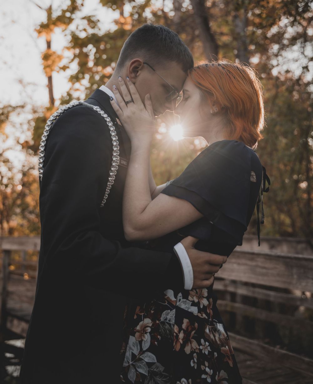 Couple sharing a romantic kiss outdoors at golden hour, surrounded by autumn trees on a wooden bridge.