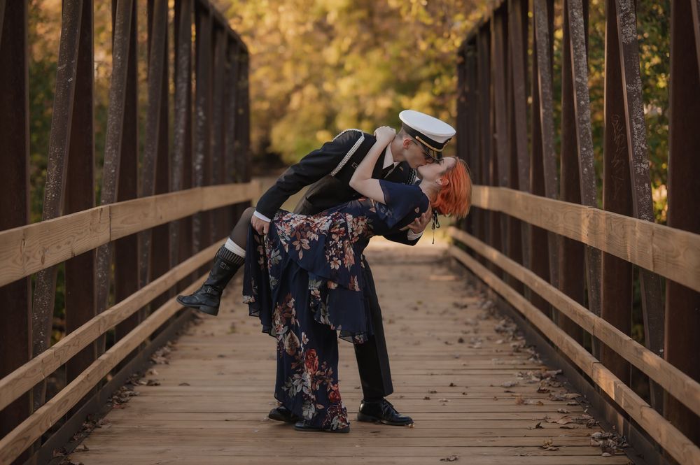 A sailor dips his partner in a romantic pose on a wooden bridge surrounded by autumn foliage.