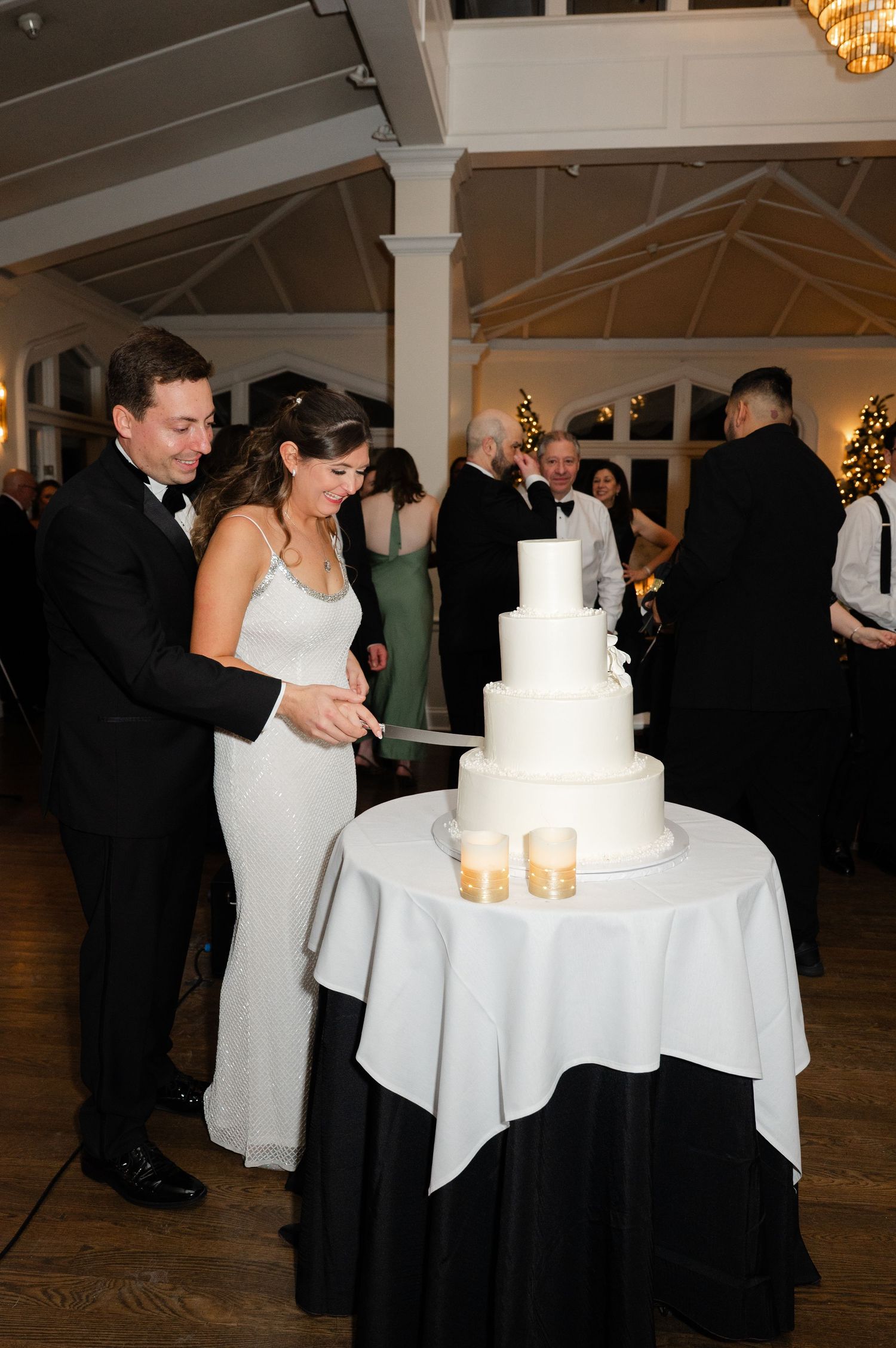 Bride and groom cutting a white four-tier wedding cake at their elegant reception venue.