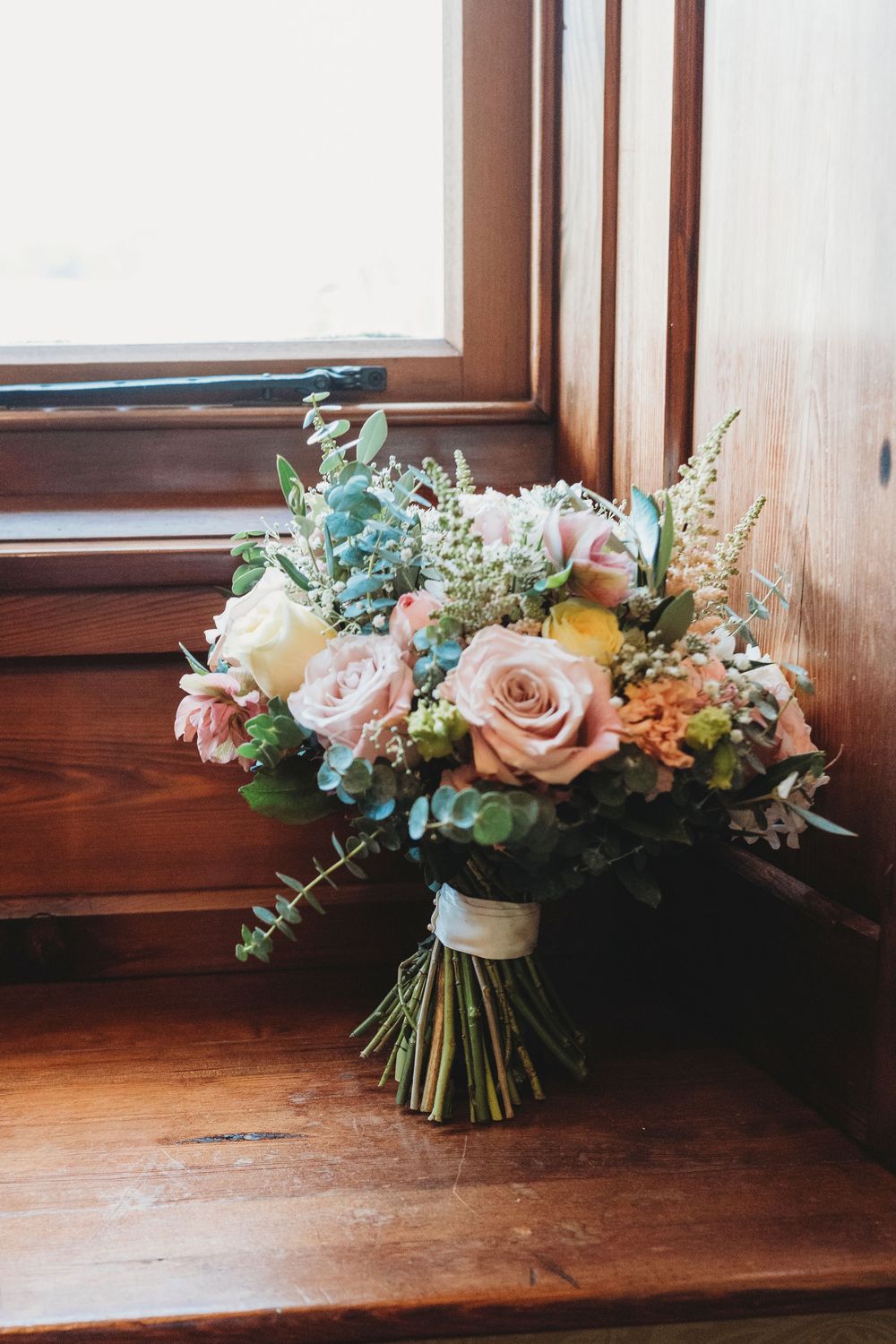 Bridal bouquet placed by window during preparations at Parc Le Breos in Gower, West Wales
