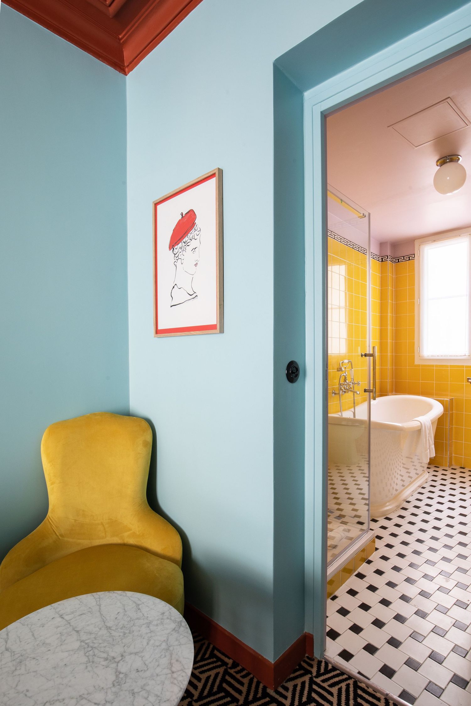 Modern bathroom interior with yellow tiles, geometric floor pattern, blue walls, and mustard yellow accent chair.