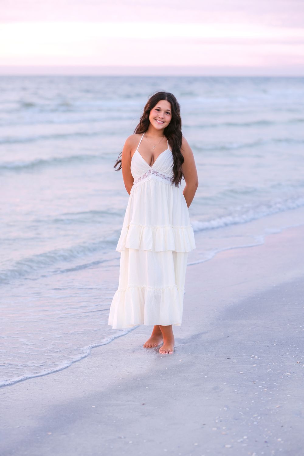 A senior girl wearing a white dress poses standing on Indian Rocks Beach at sunset for senior photos. York, Gloucester senior photographer