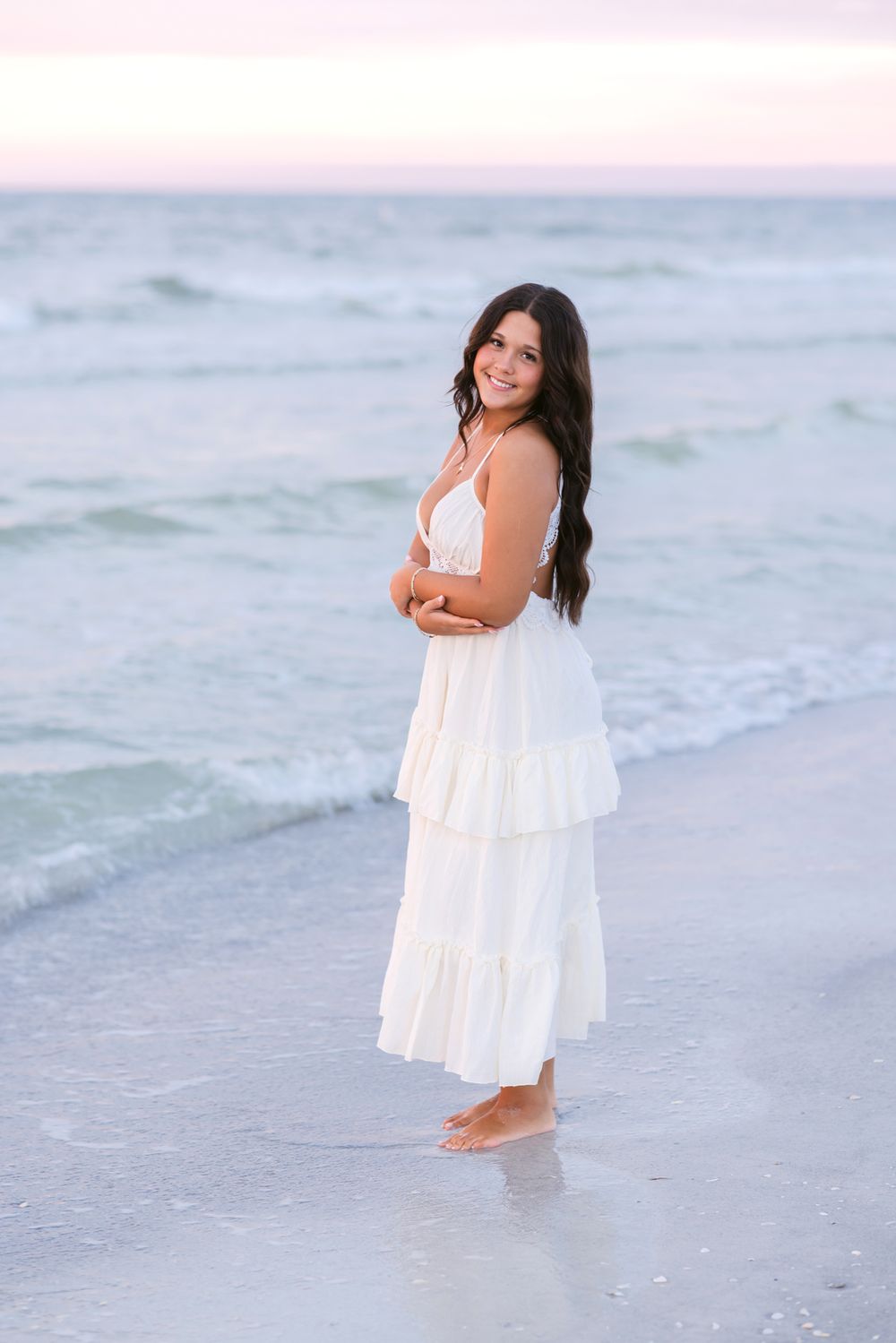A senior girl holds her arms to her chest for senior photos at Indian Rocks Beach in Florida at sunset. Kennebunkport senior photographer.