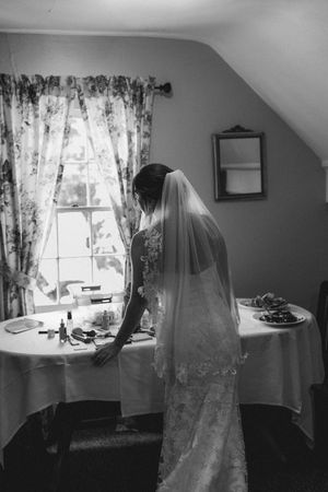 Black and white photo series showing a bride in a veil by a window with floral curtains in a sunlit room.