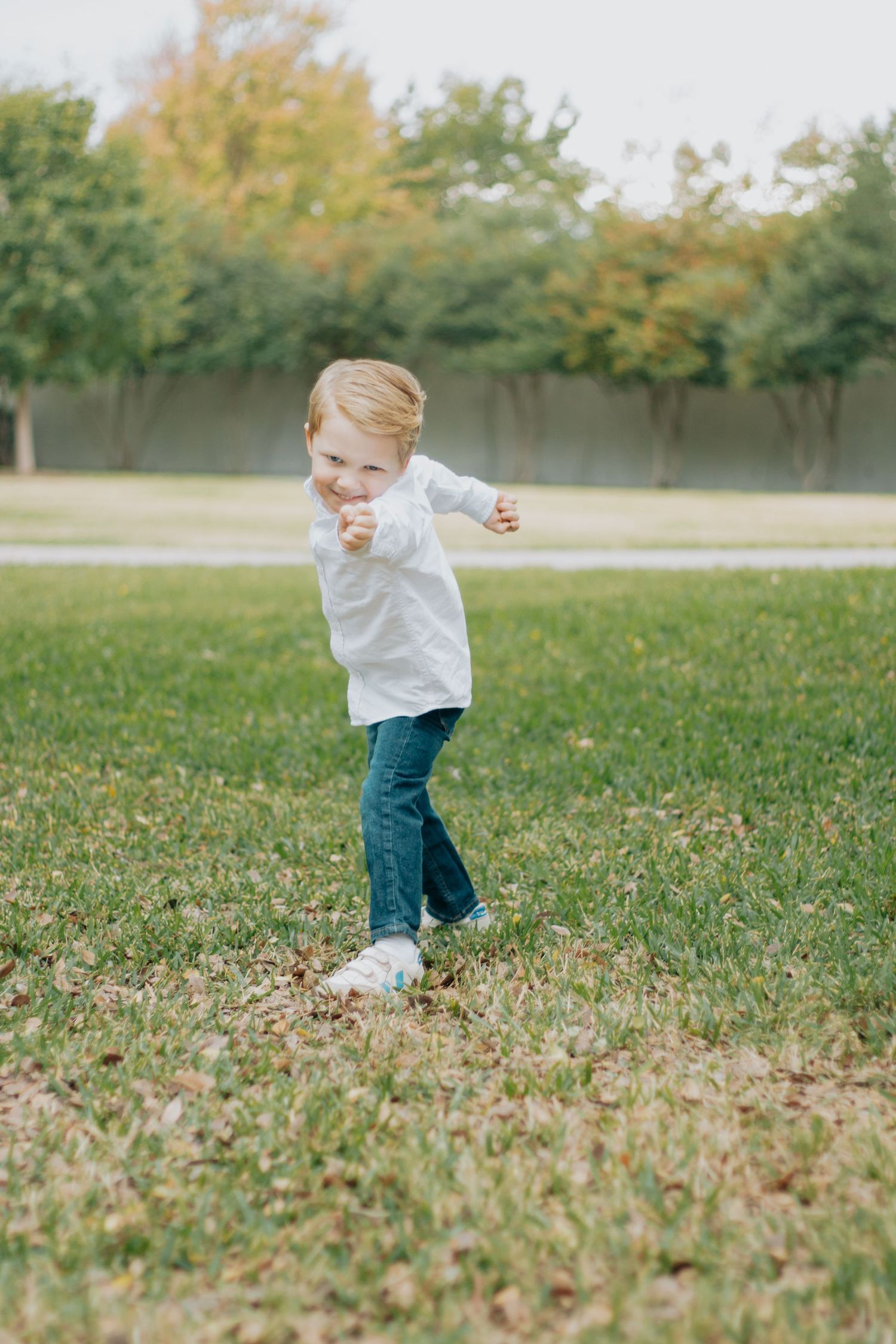 A young child in a white shirt and jeans runs joyfully through a grassy field on an autumn day.
