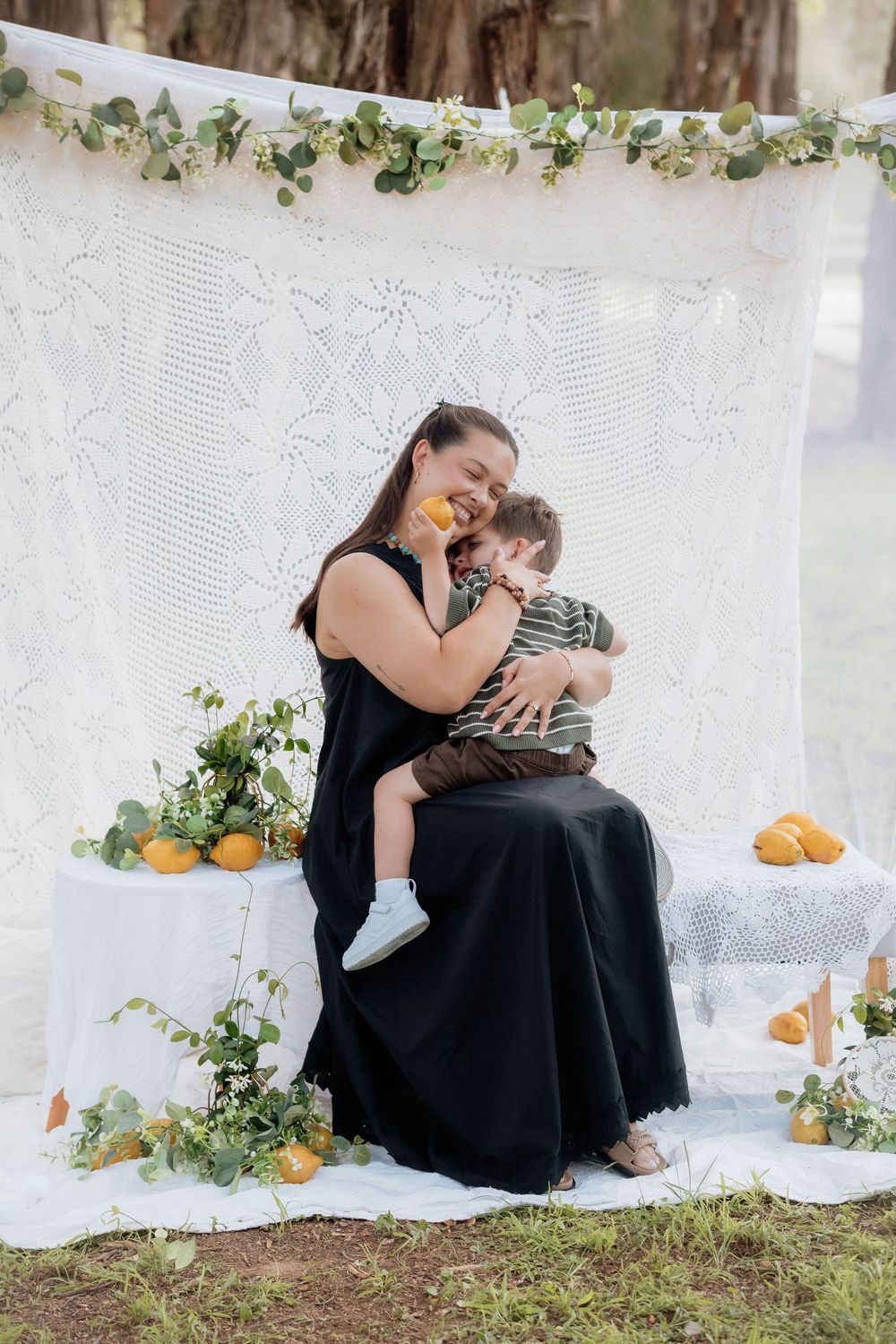 Tender family moment captured against white lace backdrop with citrus fruits and greenery decorations.