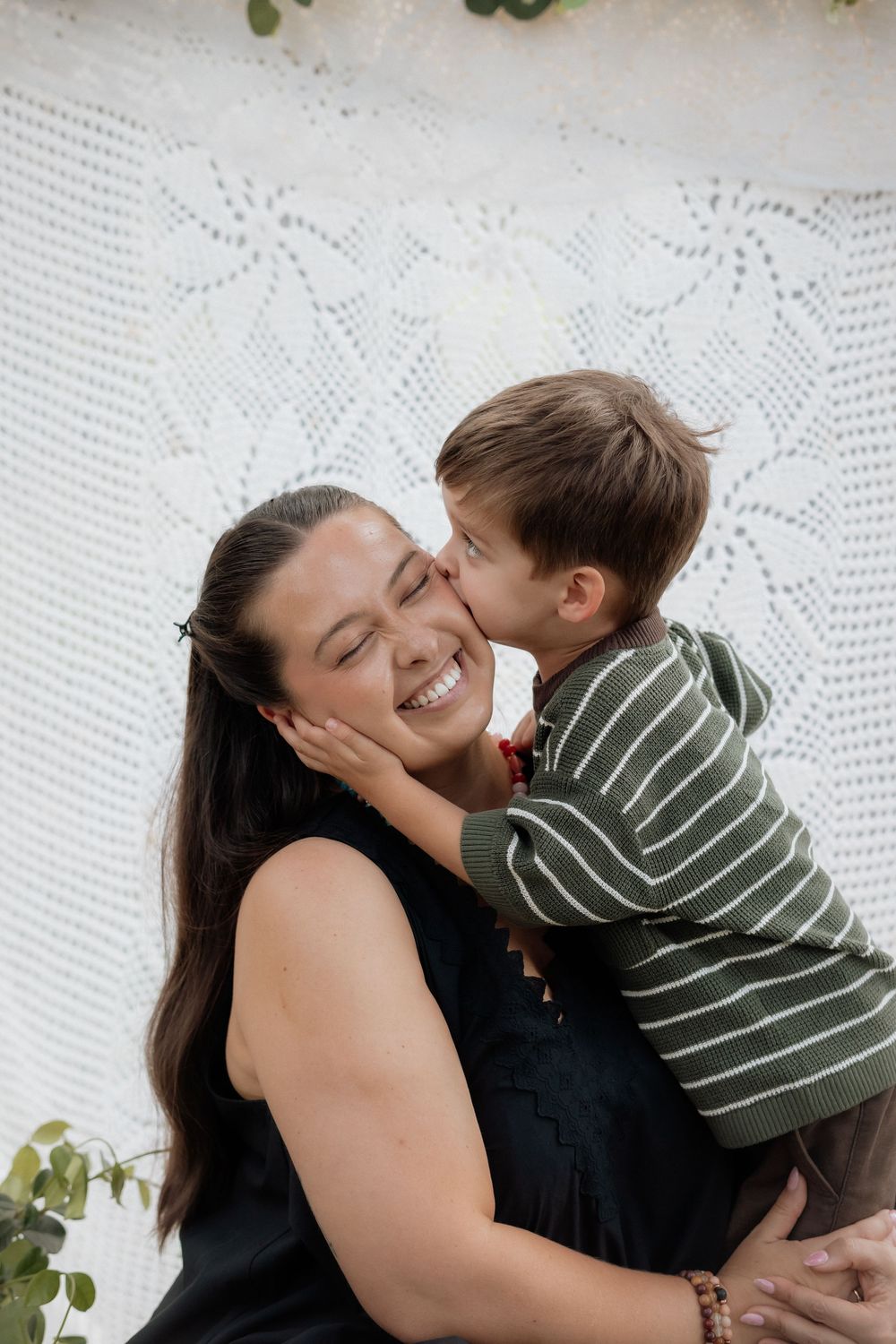 A joyful moment captured against a white lace backdrop as a small child in stripes gives a sweet kiss.