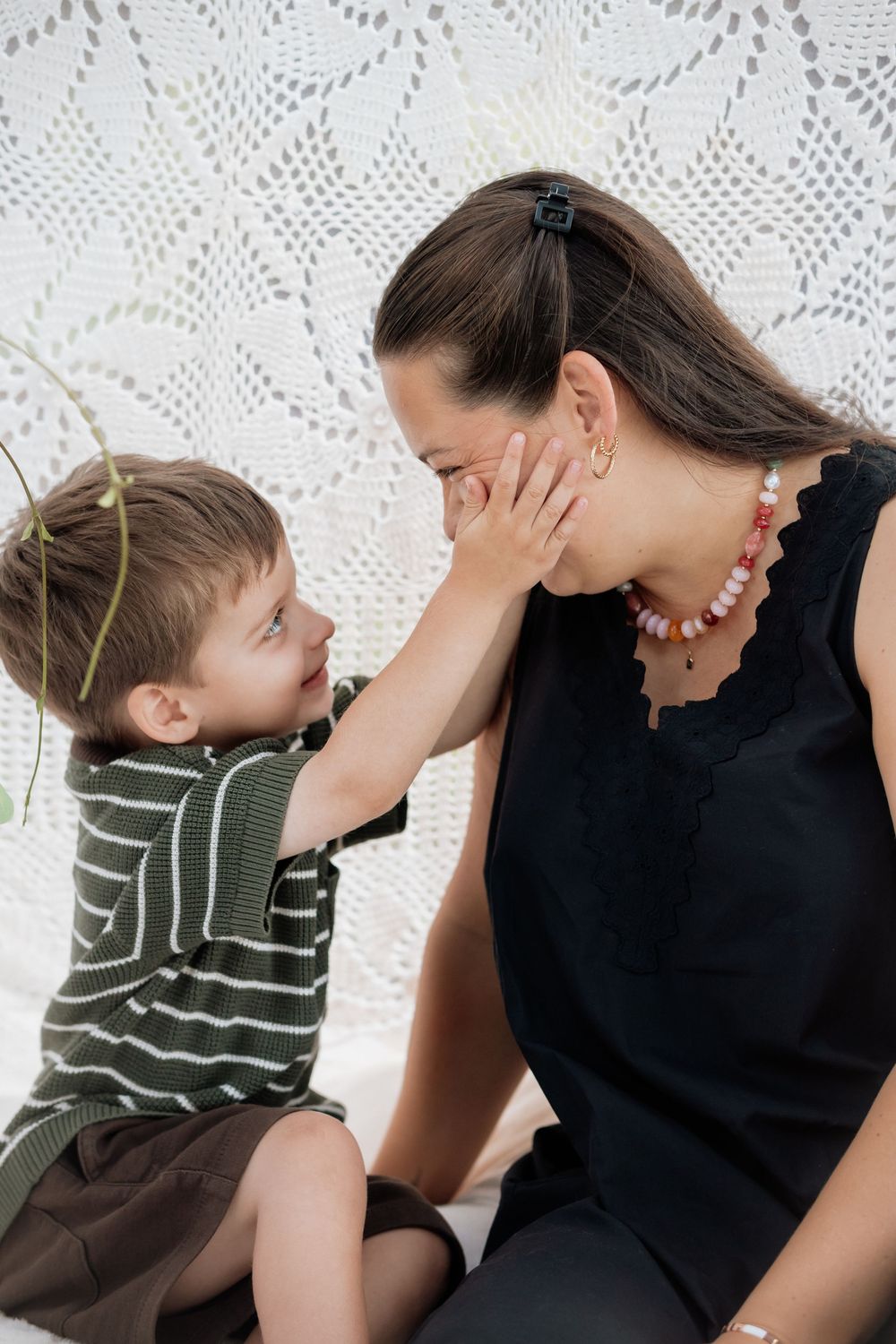 A touching moment between a child in a striped shirt and woman in black against a white lace backdrop.