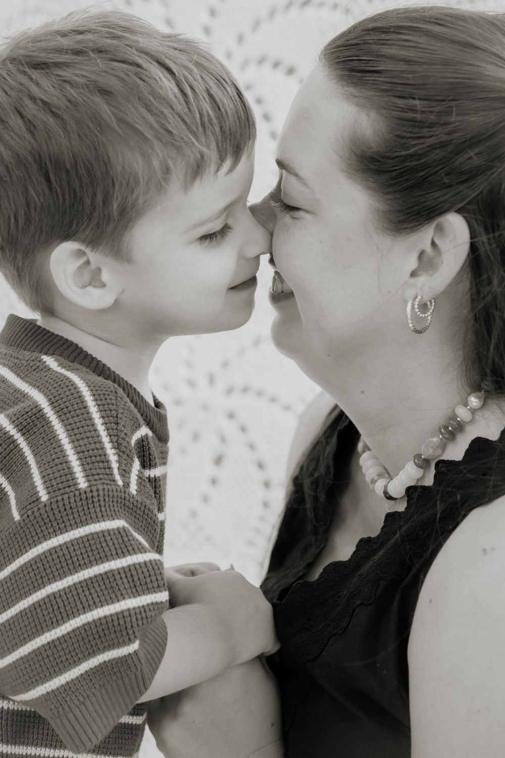 A tender black and white portrait shows an intimate moment between parent and child sharing a gentle nose touch.