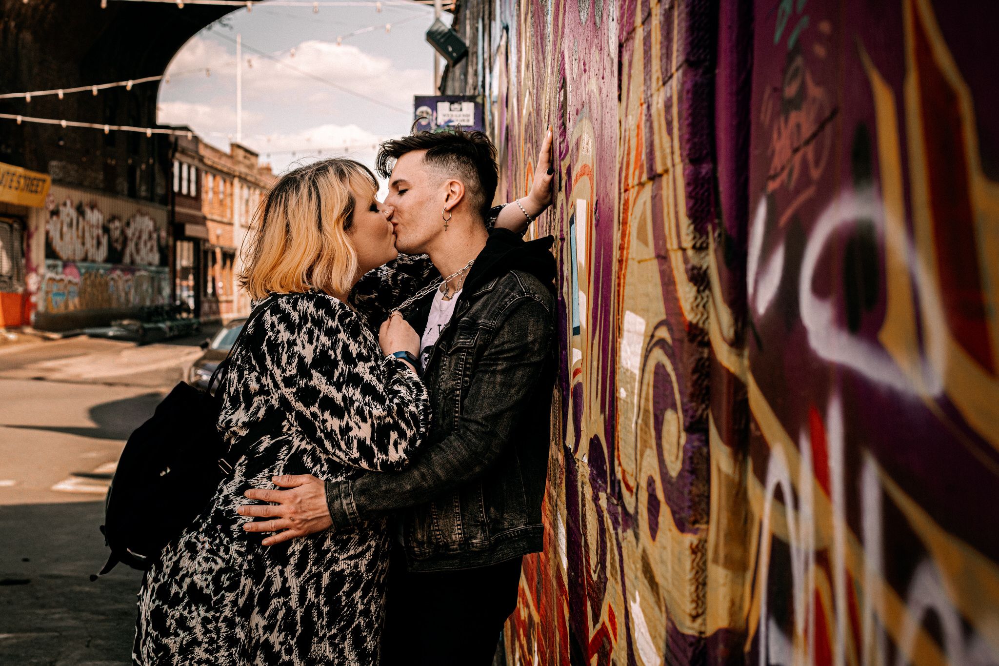 A romantic couple embraces near colorful street art murals in an alleyway.
