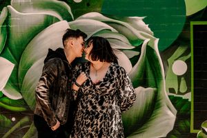 A romantic moment captured against a green floral mural backdrop with artistic swirls and patterns.