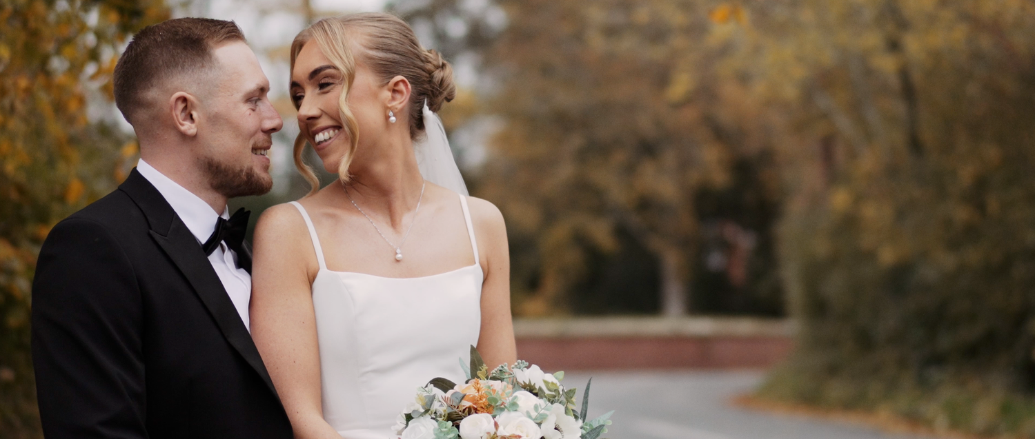 Romantic outdoor autumn wedding portrait with couple embracing on tree-lined path.