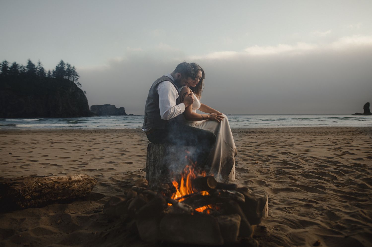 A couple poses for wedding photos against a dramatic mountain backdrop with evergreen trees and a scenic lake.