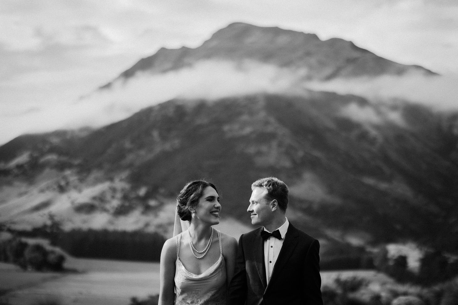 A black and white wedding photo of a newlywed couple against mountain landscapes at Lookout Lodge, Wanaka, Otago, New Zealand.